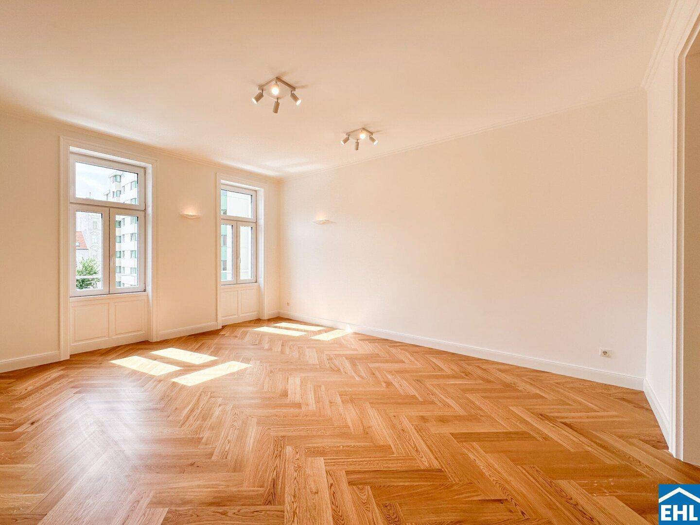 Helles Wohnzimmer mit klassischem Fischgrätparkett und großen Fenstern, die viel Sonnenlicht hereinlassen.