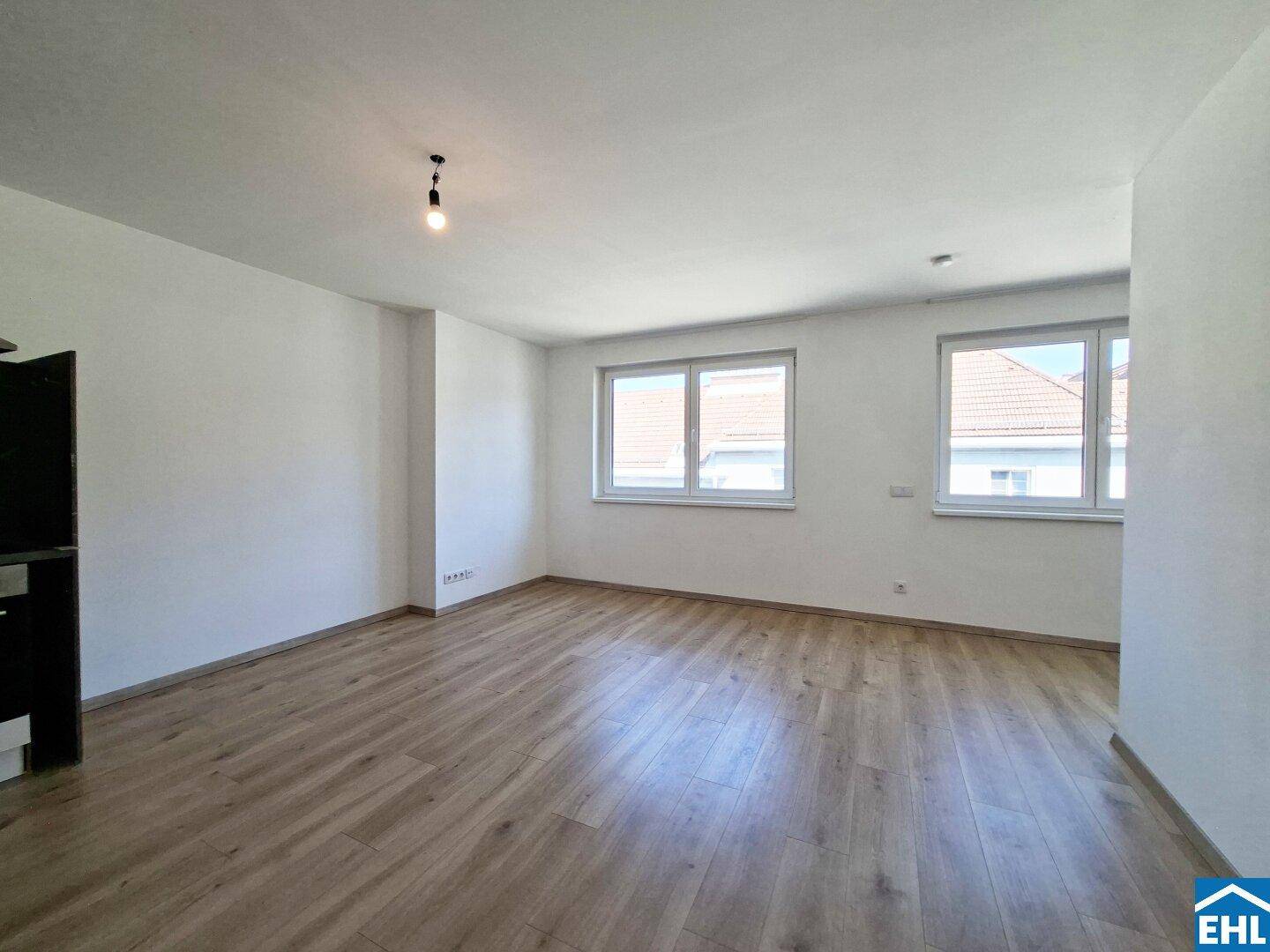 Lichtdurchfluteter Wohnbereich mit großen Fenstern und neuem Laminatboden.