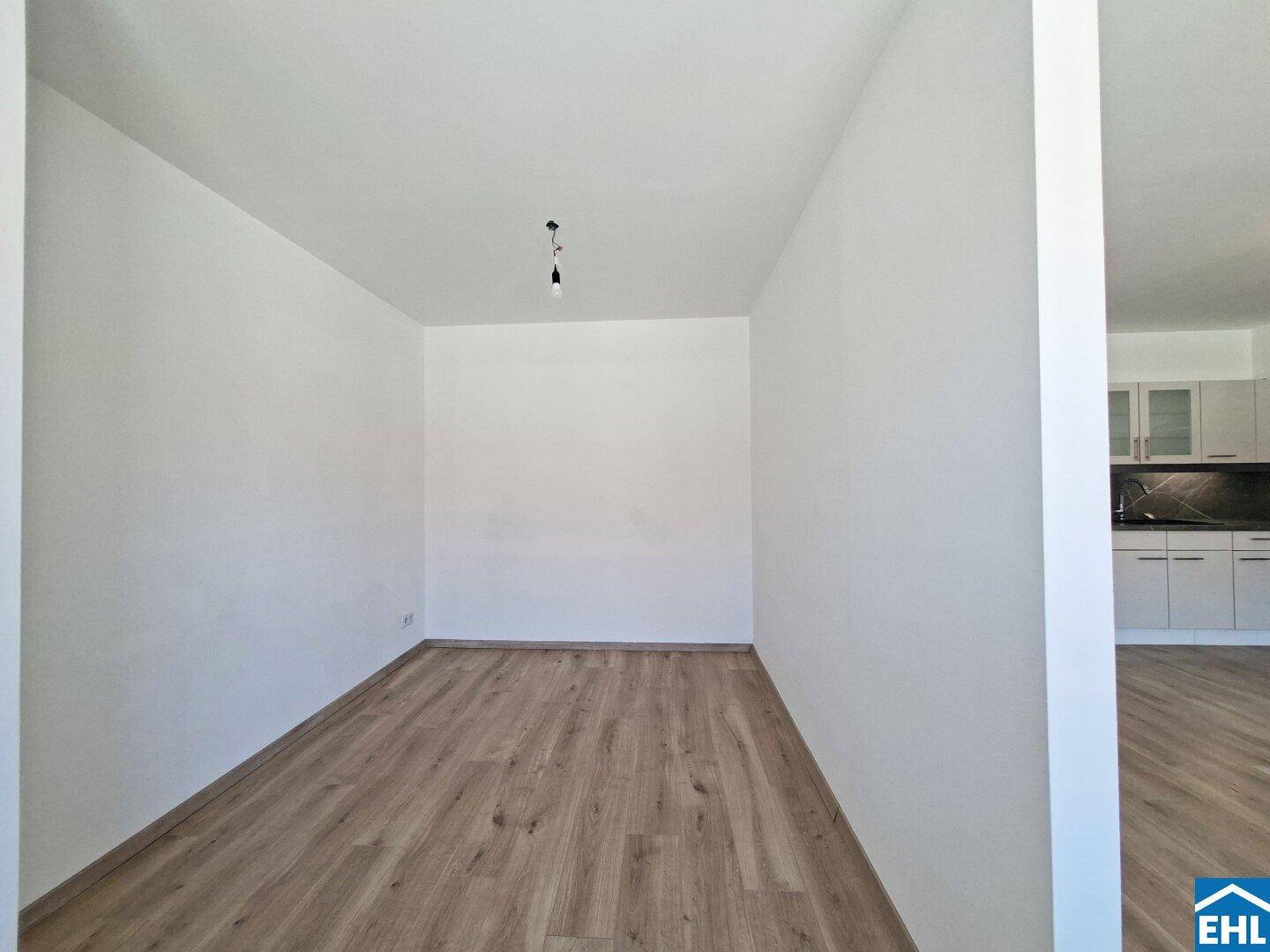 Leeres Zimmer mit hellem Laminatboden und weißen Wänden, bereit zur individuellen Gestaltung.