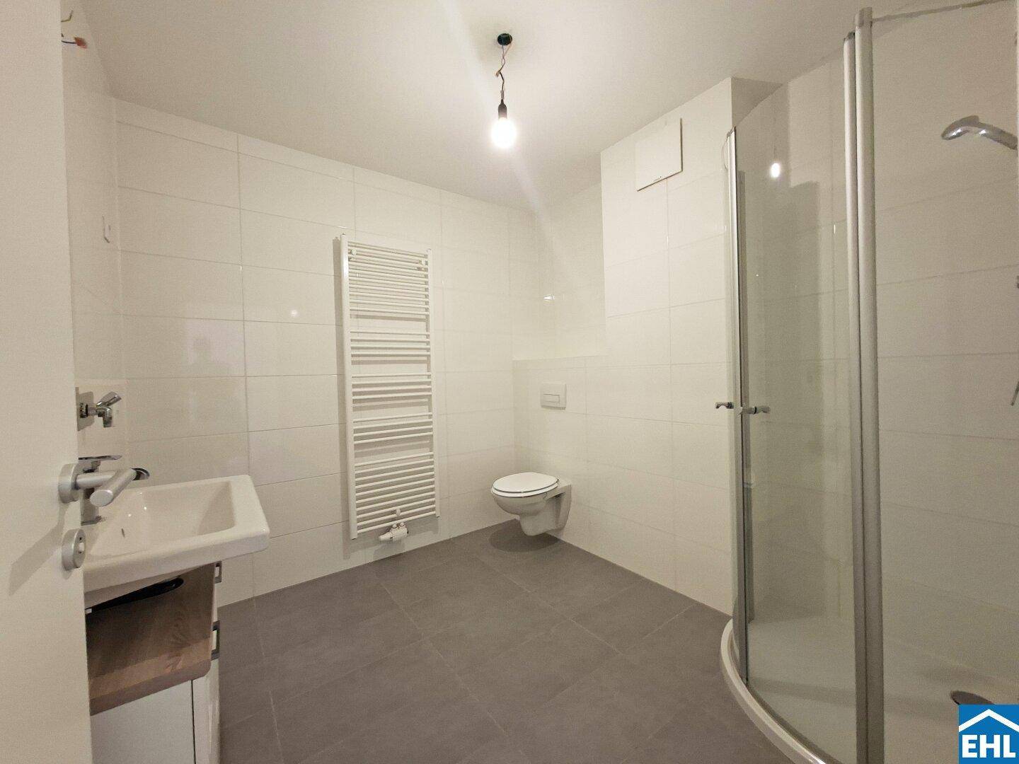Modernes Badezimmer mit weißen Fliesen, Dusche, WC und beheiztem Handtuchhalter.