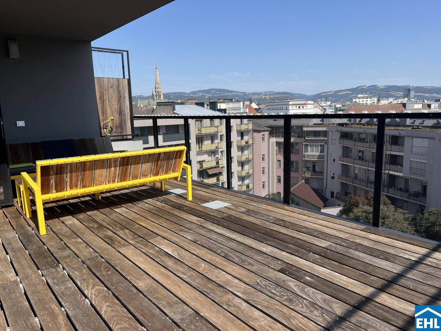 Geräumige Holzterrasse mit einer gelben Sitzbank und Panoramablick über die Stadt.
