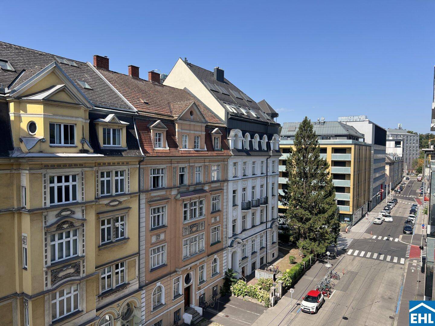 Blick auf eine belebte Stadtstraße mit einer Mischung aus Alt- und Neubauten unter blauem Himmel.