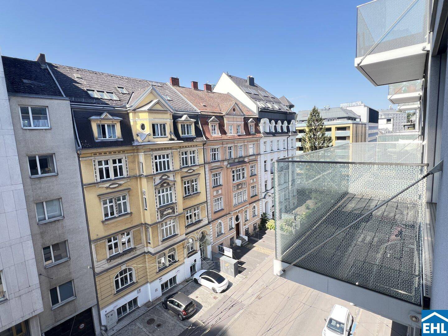 Weitblick von einem Balkon auf eine Stadtstraße mit Gebäuden und parkenden Autos.