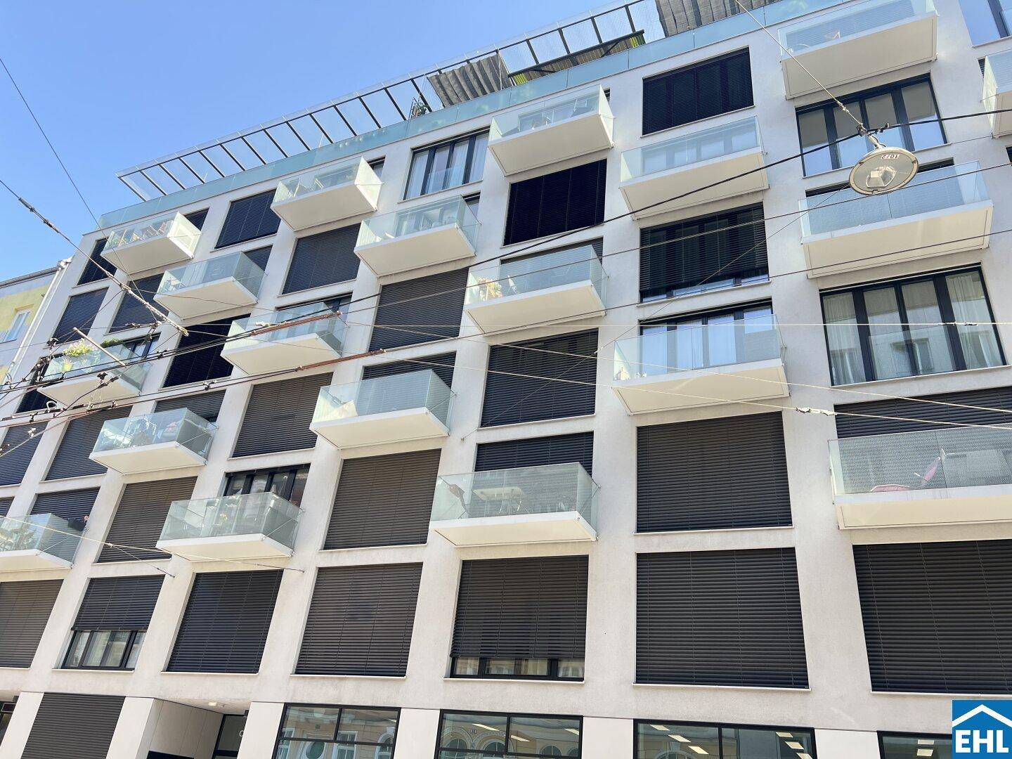 Ansicht einer modernen Wohnfassade mit vielen Balkonen und dunklen Fensterläden.
