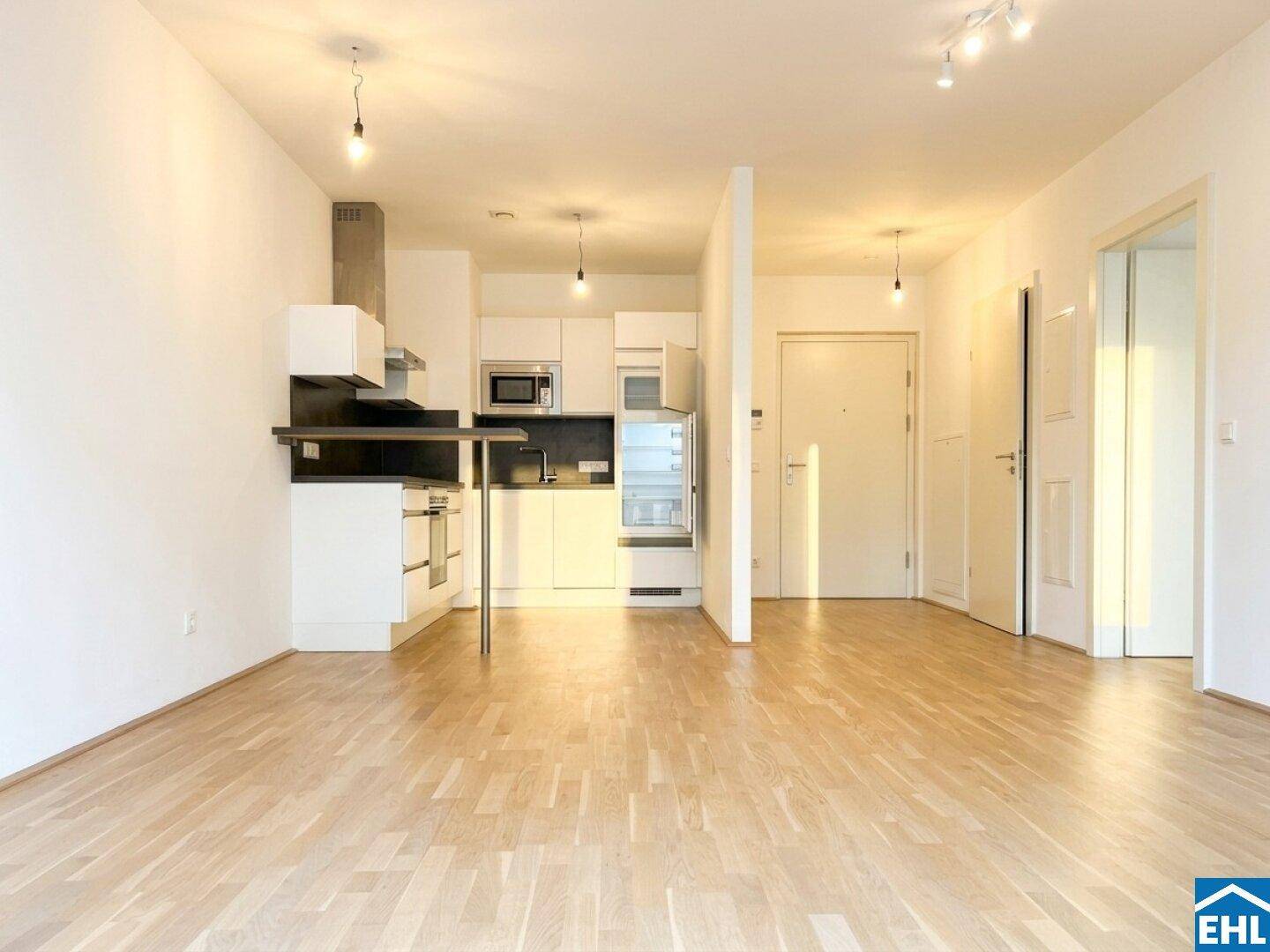 Heller, leerer Wohnbereich mit offener Küchenzeile und Parkettboden in einem Neubau.