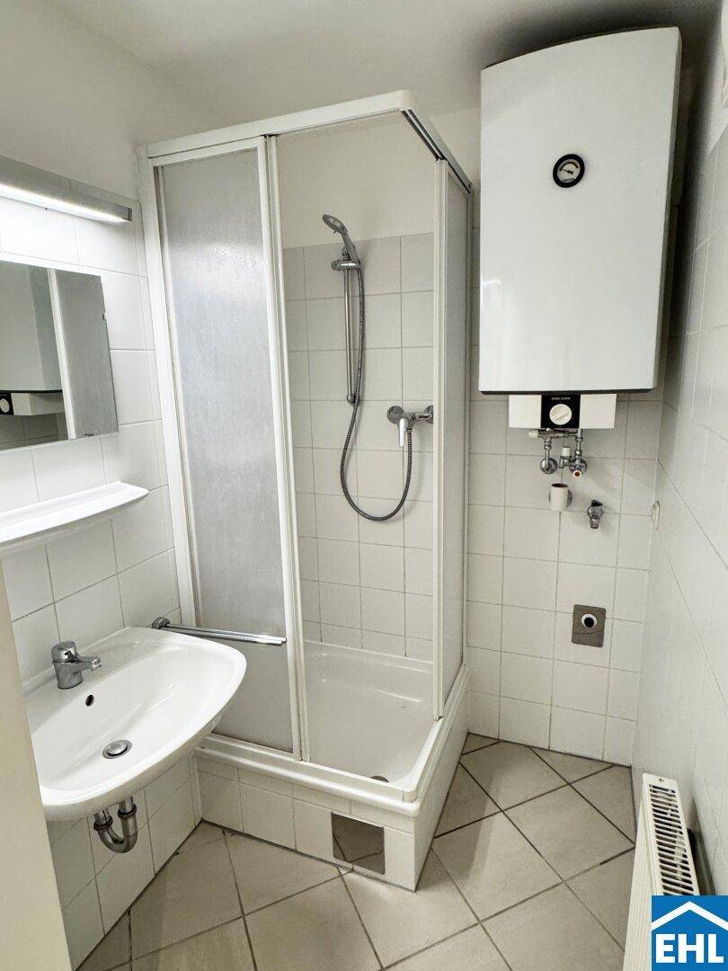 Kleines Badezimmer mit Duschkabine, Waschbecken und Wandheizkörper, komplett gefliest.
