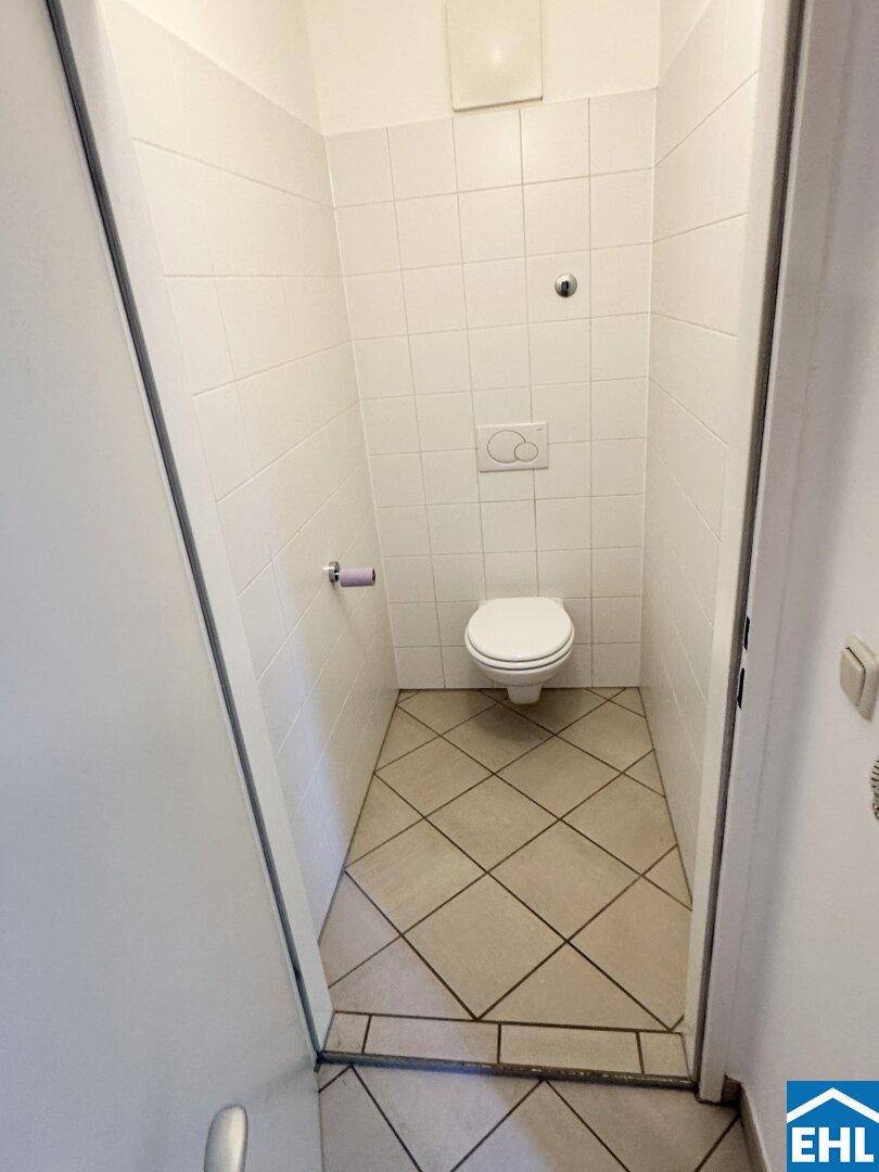Separates WC mit Wandtoilette und Fliesenboden, in schlichtem Design gehalten.