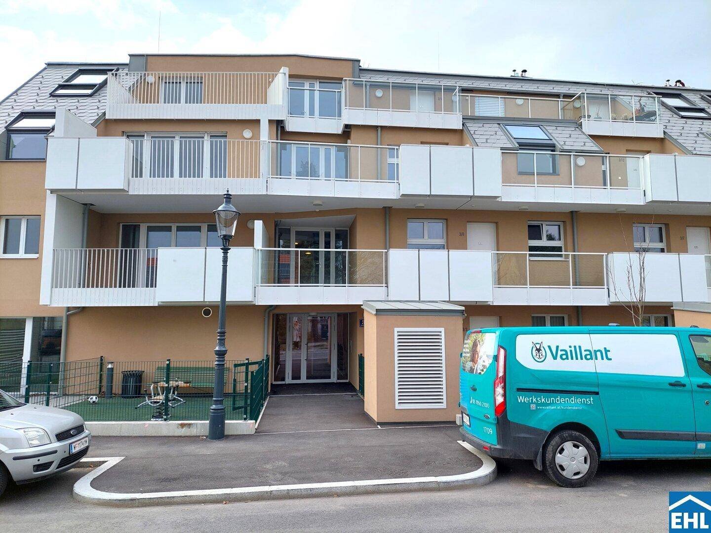 Fassade eines modernen Wohngebäudes mit Balkonen und Eingangsbereich an einem bewölkten Tag.