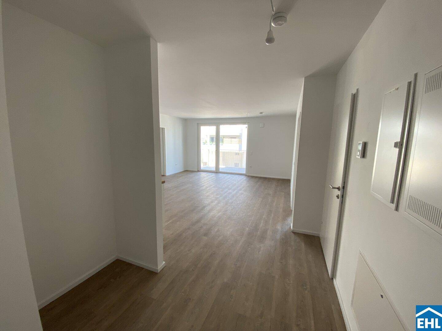 Heller Flur mit Laminatboden, der zu einem lichtdurchfluteten Wohnbereich mit Balkonzugang führt.