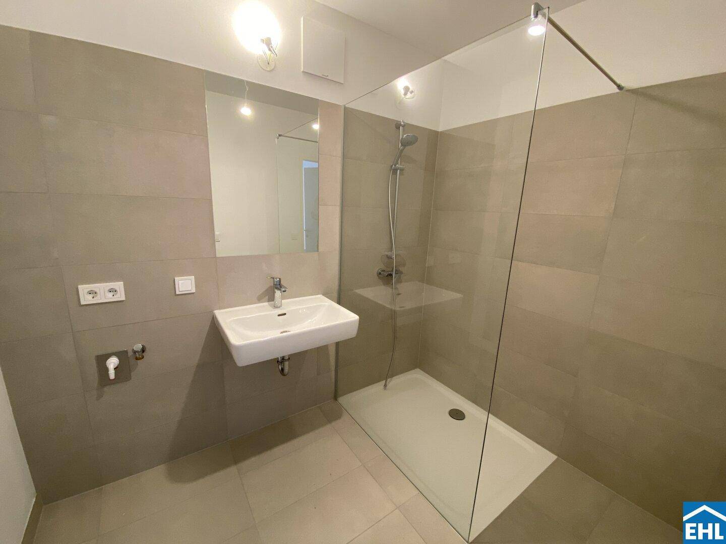 Modernes Badezimmer mit großformatigen Fliesen, ebenerdiger Dusche und wandhängendem Waschbecken.