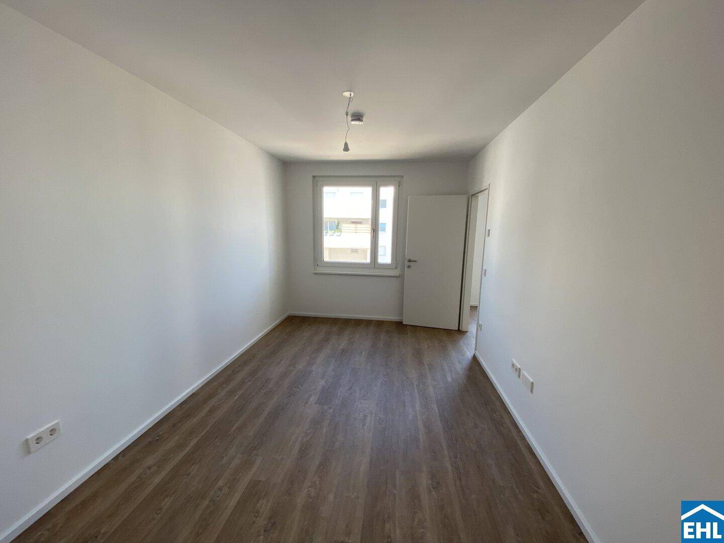 Freundliches, leeres Zimmer mit Laminatboden und großem Fenster, ideal als Schlaf- oder Arbeitszimmer.