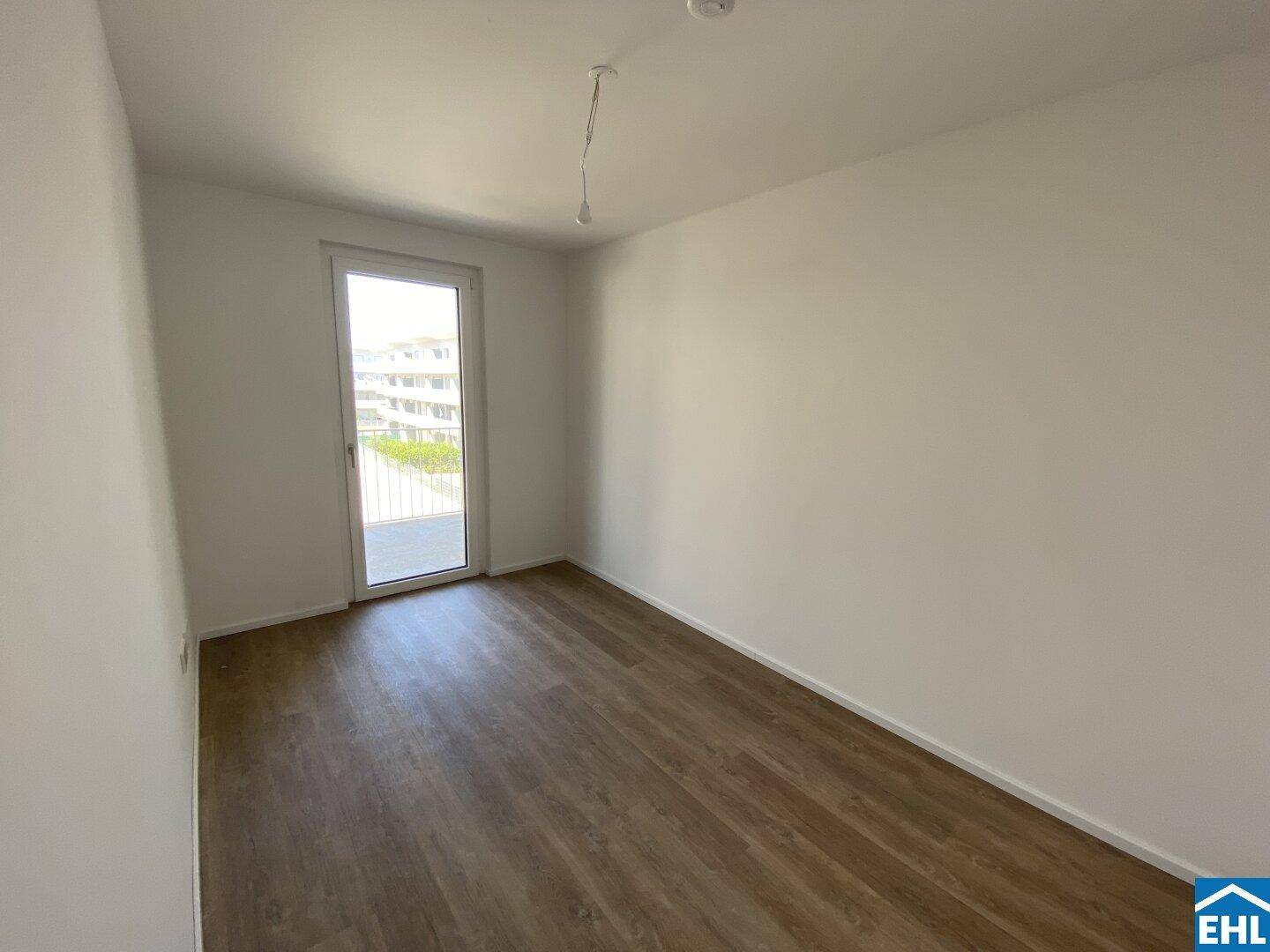 Helles Zimmer mit Laminatboden und Zugang zu einem Balkon, ideal für ein Schlafzimmer.