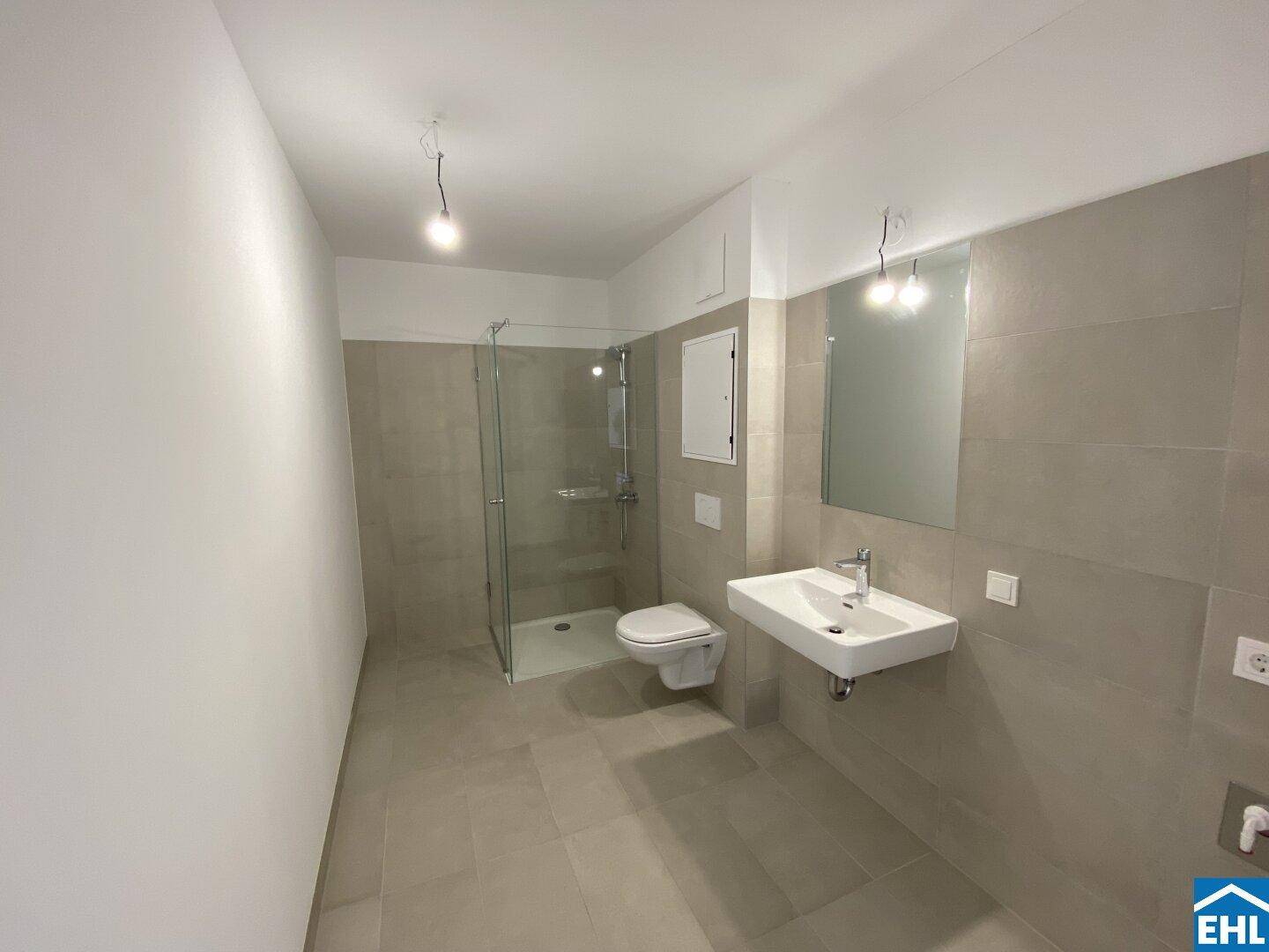 Modernes Badezimmer mit grauen Fliesen, ebenerdiger Dusche und Wand-WC.
