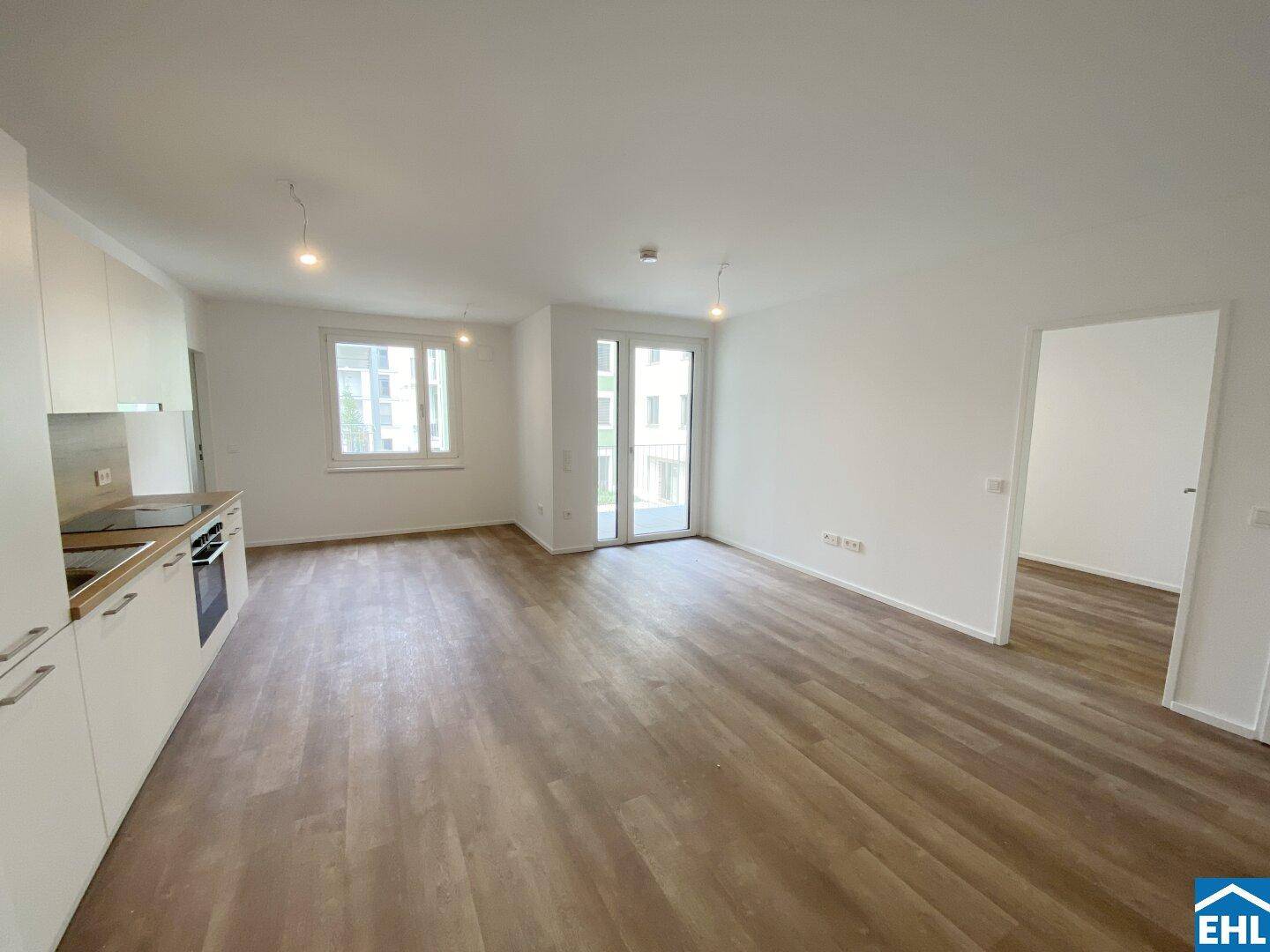 Geräumiger Wohn-Essbereich mit moderner Einbauküche und hellem Laminatboden.