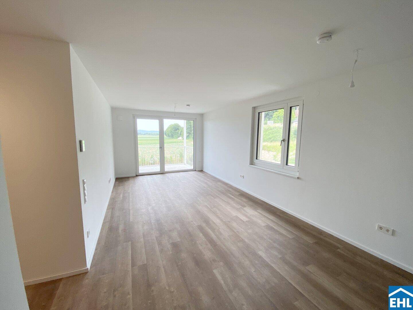 Geräumiger Wohnbereich mit großen Fenstern, Zugang zum Balkon und Blick ins Grüne.