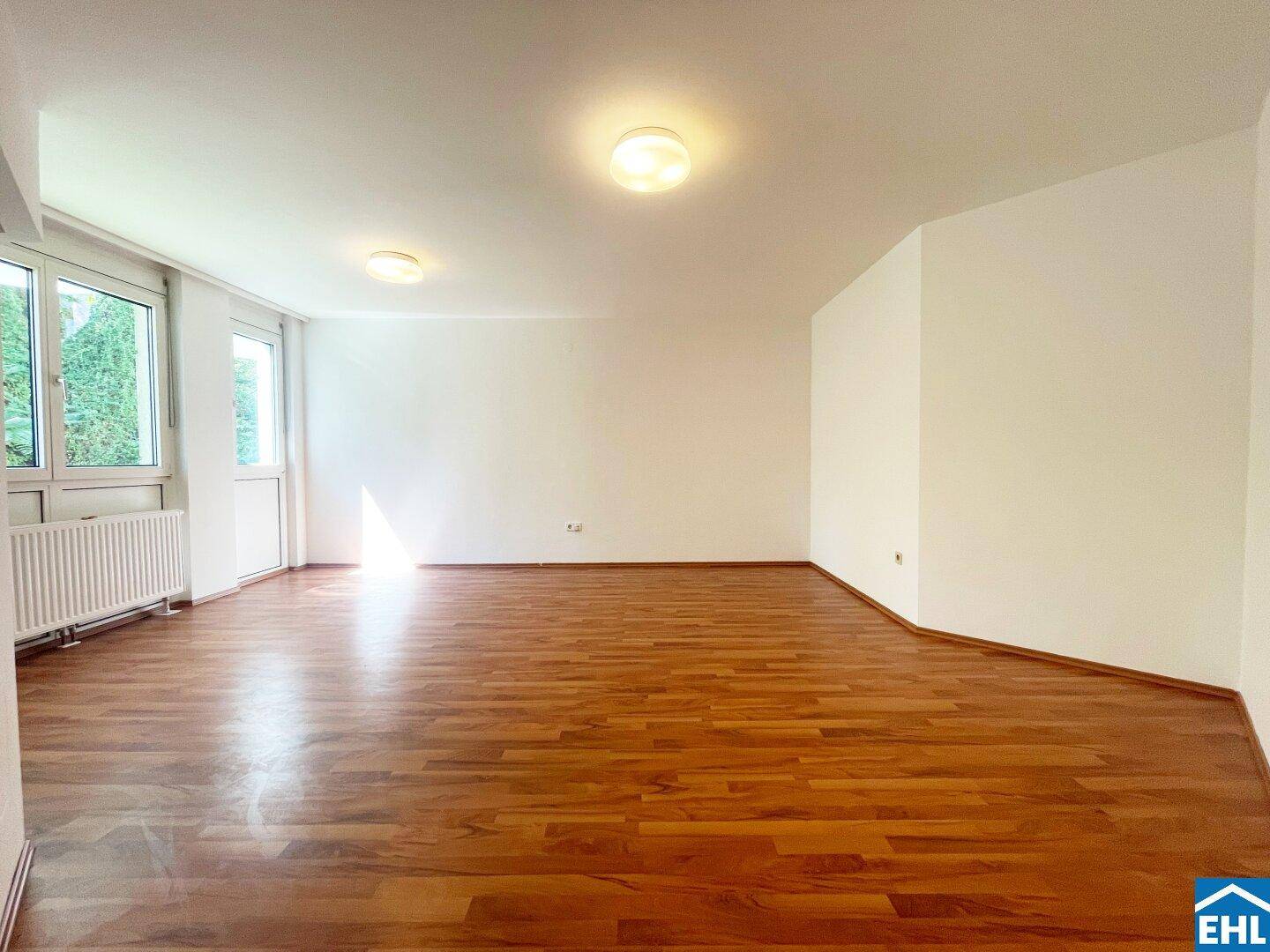 Geräumiges, helles Zimmer mit Laminatboden und großen Fenstern, ideal für vielfältige Nutzung.