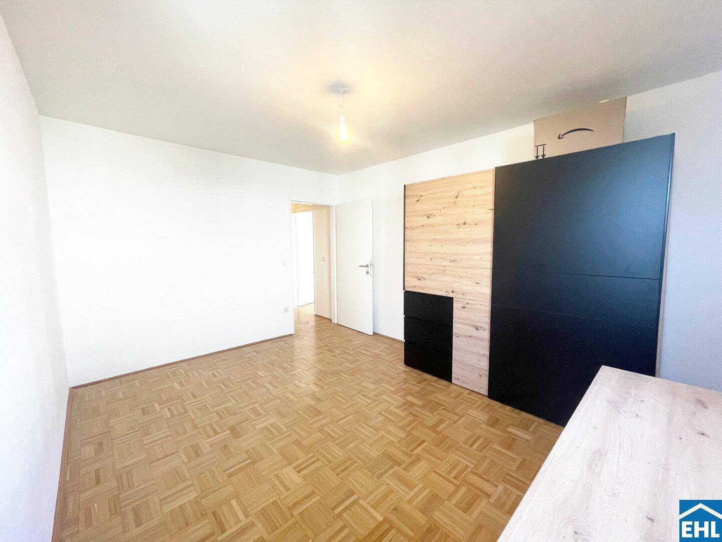 Schlafzimmer mit Parkettboden und modernen Holz-Schwarz-Schränken, bietet viel Stauraum.