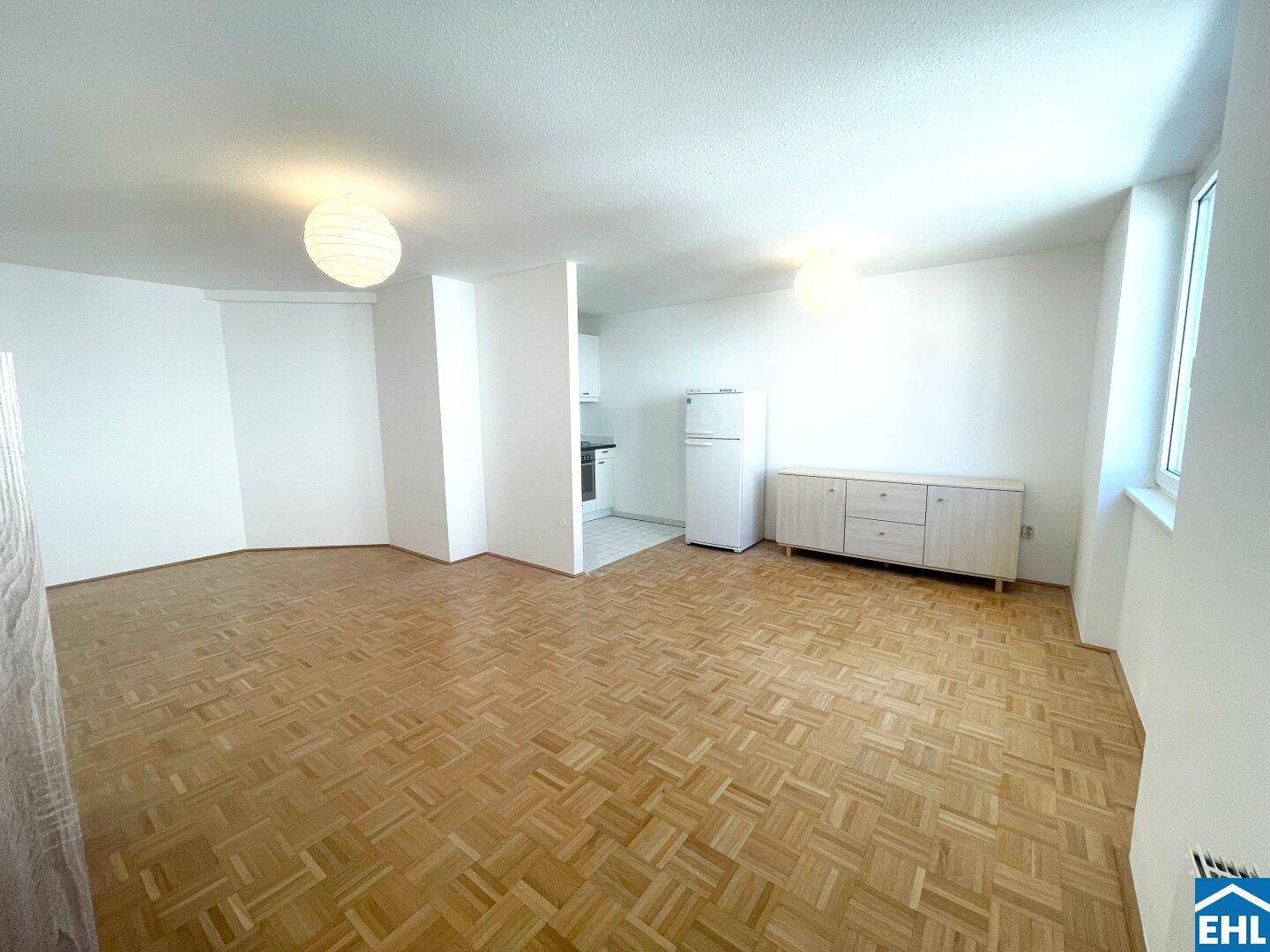 Offener Wohnbereich mit Parkettboden, integrierter Küche und einem Sideboard.