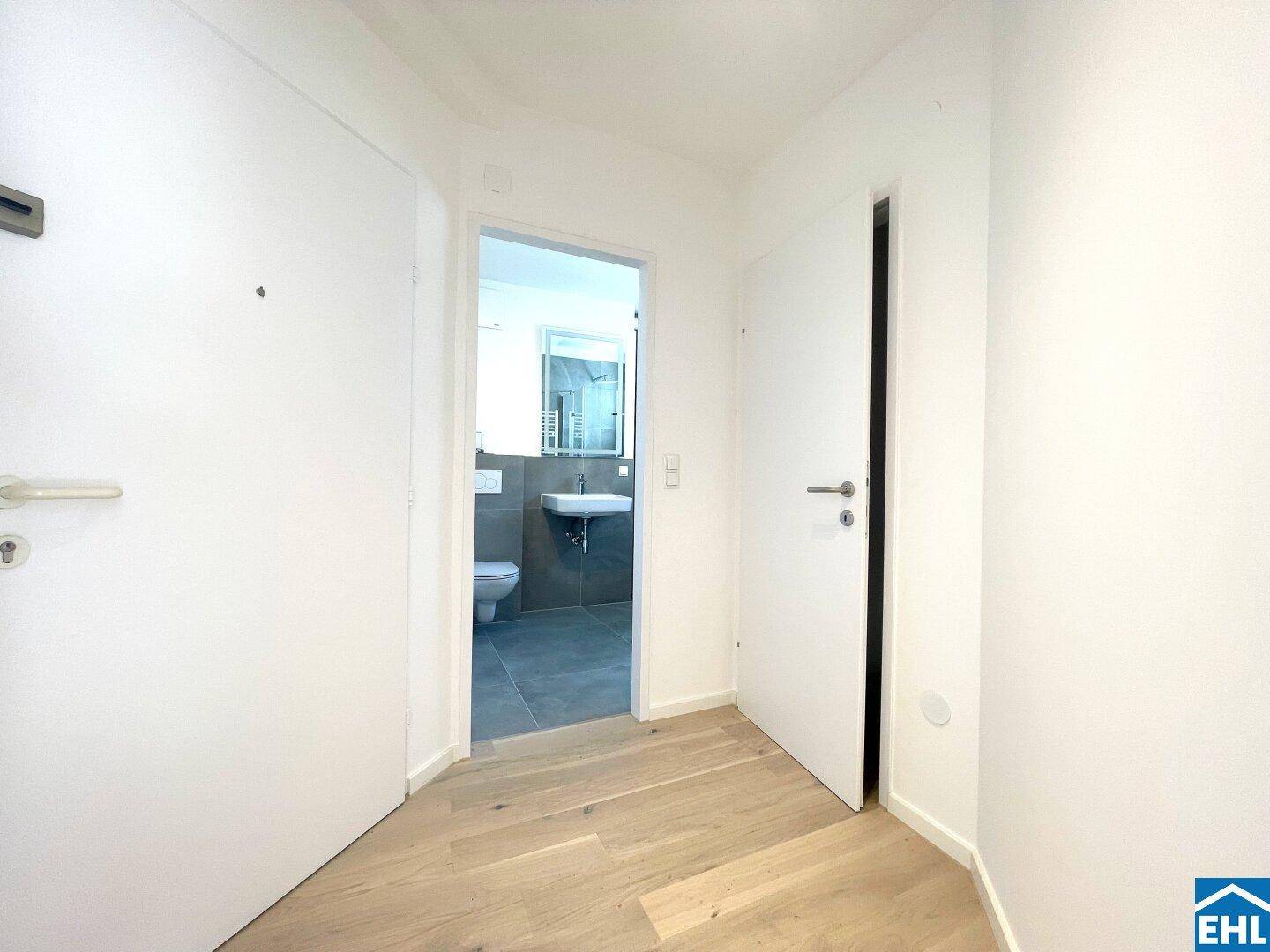 Heller Flur mit Holzboden und Zugang zum modernen Badezimmer.