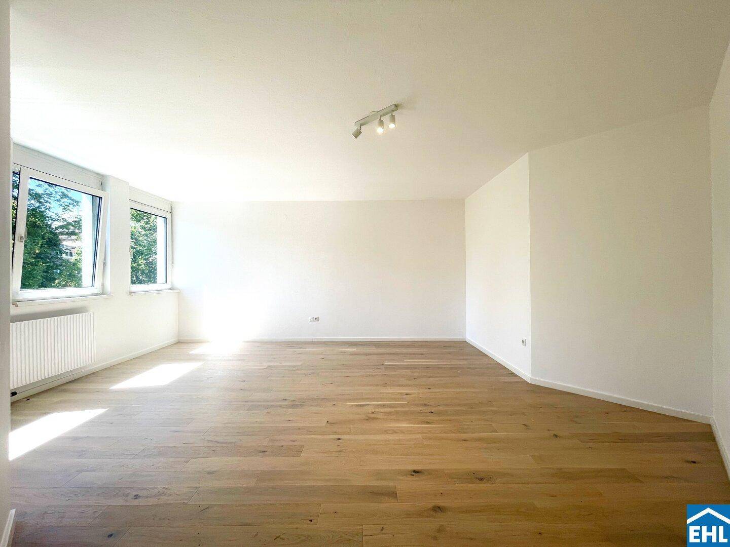 Helles Wohnzimmer mit großen Fenstern, Holzboden und viel Tageslicht.