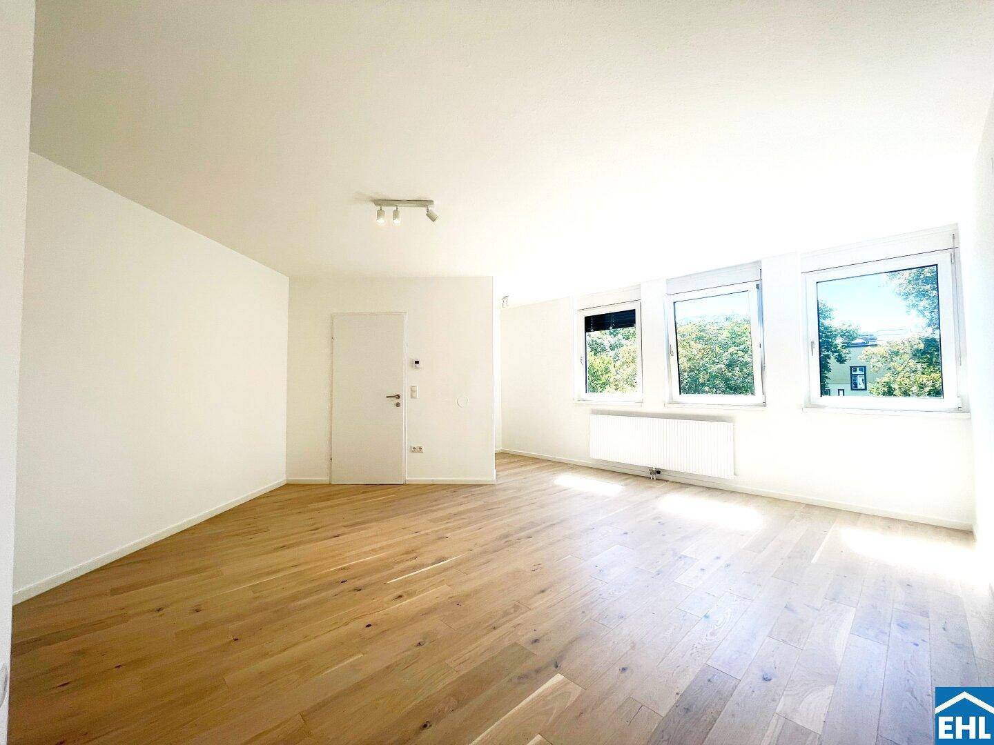 Geräumiges Wohnzimmer mit Holzboden und Blick ins Grüne durch die Fenster.