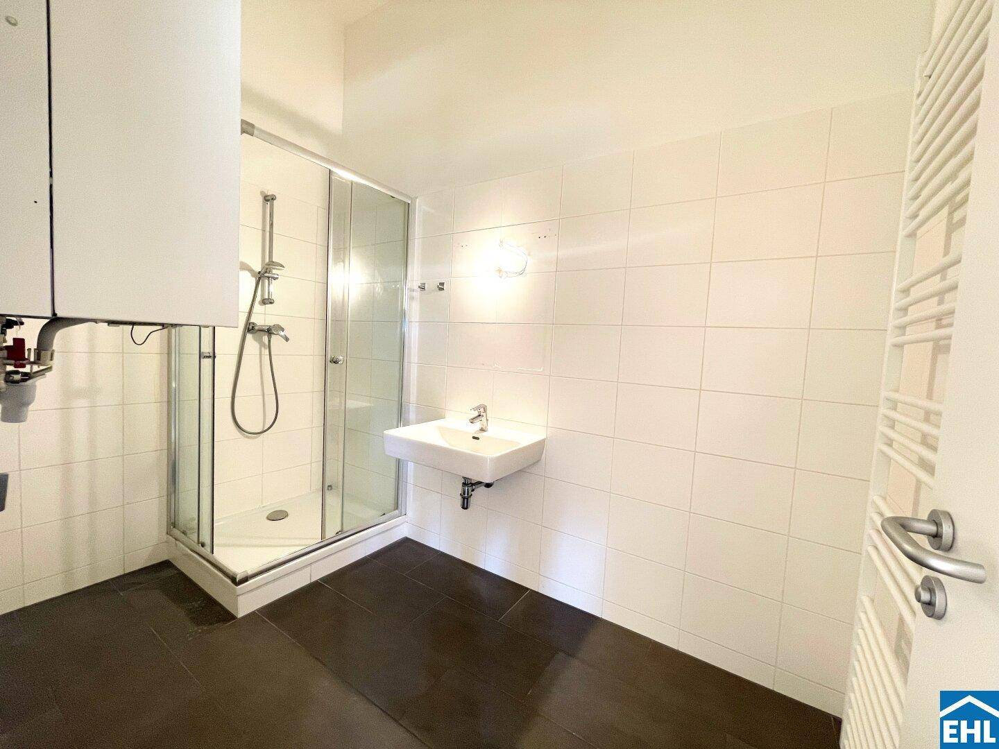 Badezimmer mit Duschkabine, Waschbecken, beheiztem Handtuchhalter und weißen Wandfliesen.