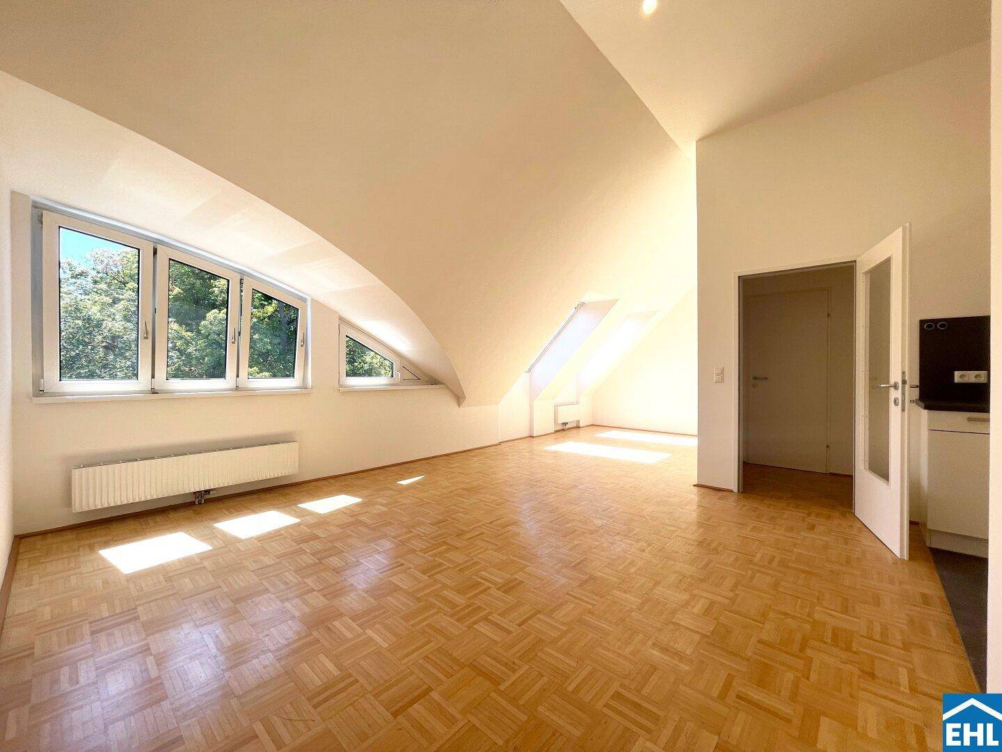 Lichtdurchflutetes Dachgeschosszimmer mit Parkettboden, schrägen Wänden und großen Fenstern.
