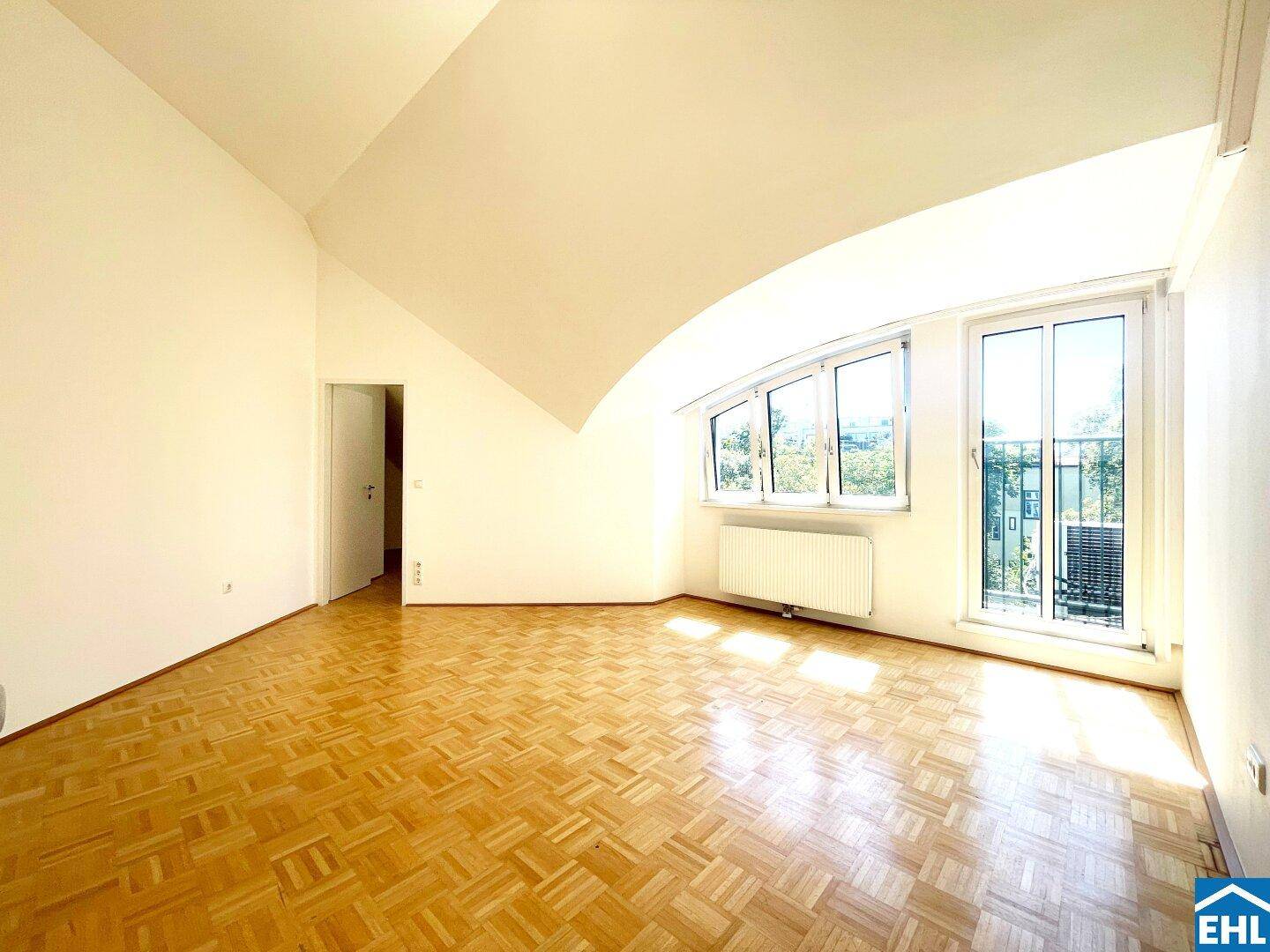 Heller Wohnraum mit Parkettboden, schrägen Wänden und Fenstern mit Blick ins Freie.