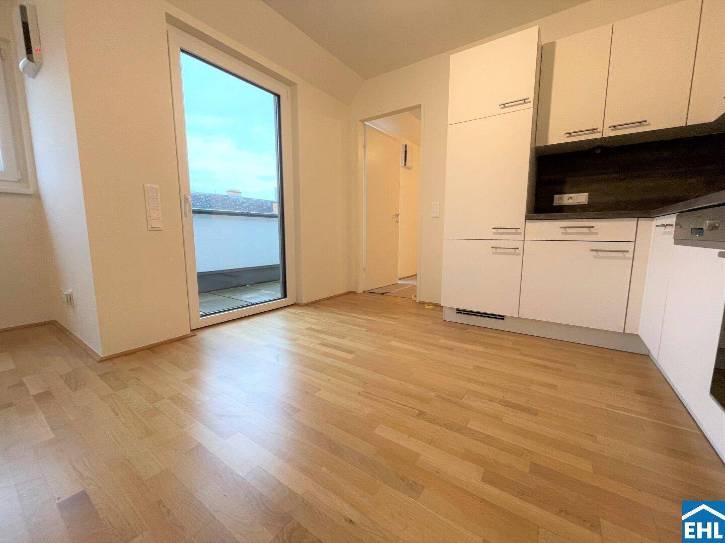 Helle Küche mit weißen Einbauschränken, Holzboden und direktem Zugang zu einem Balkon.