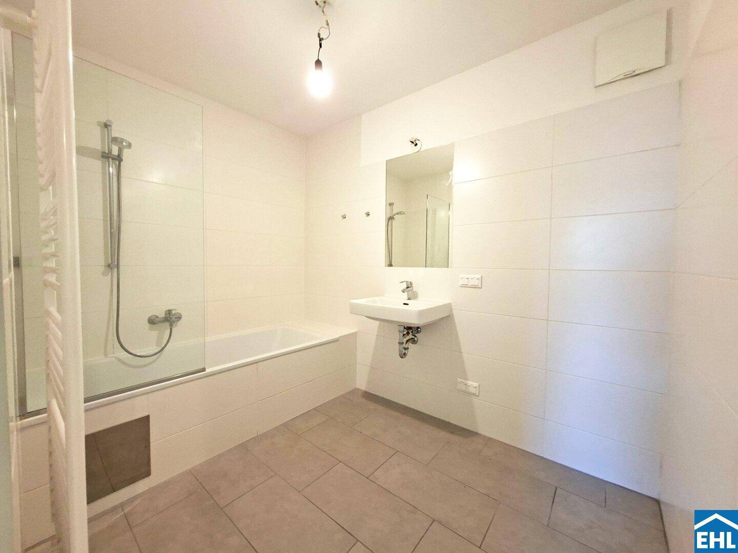 Modernes Badezimmer mit Badewanne, Duschwand, Wandwaschbecken und hellen Fliesen.