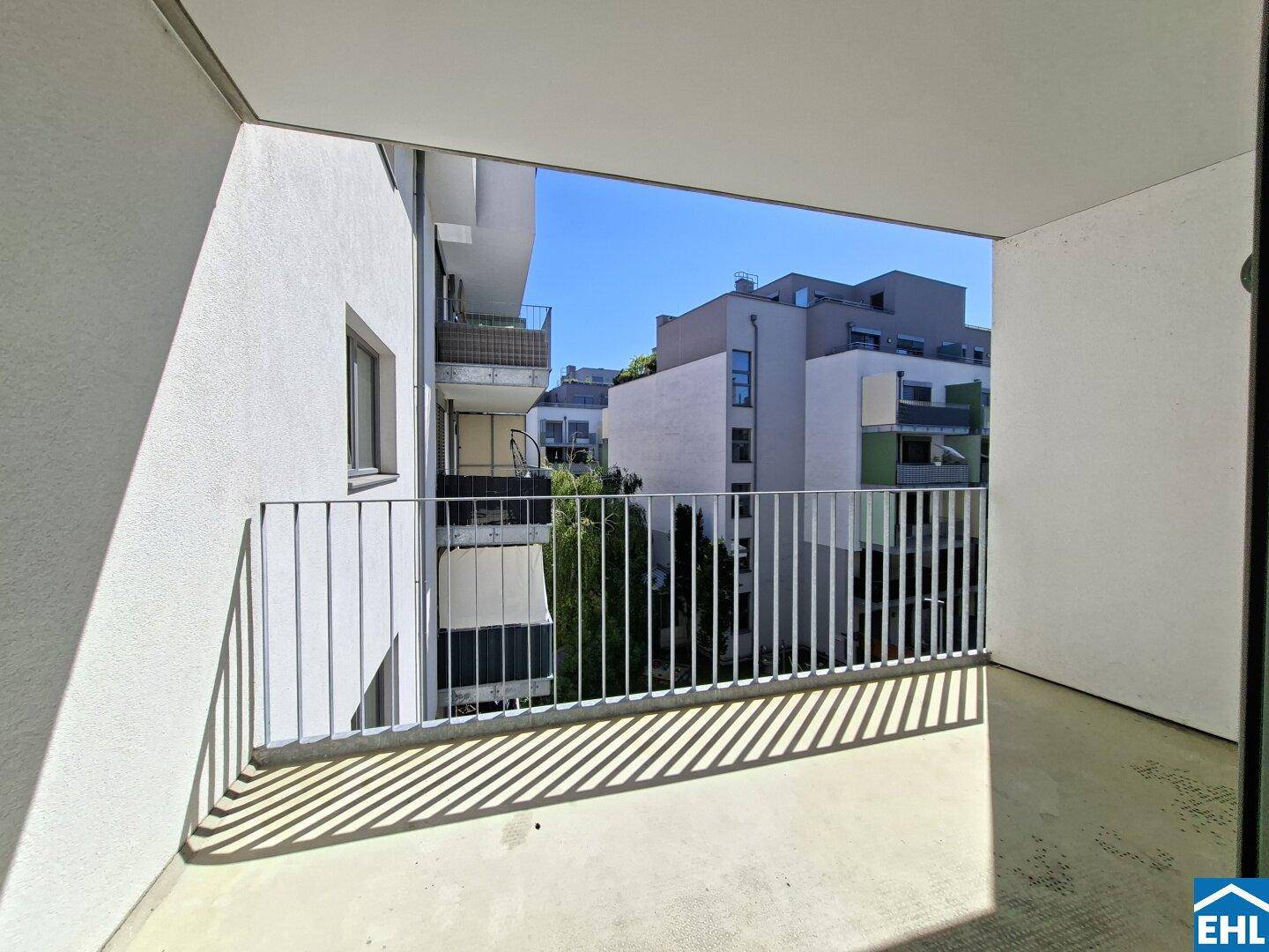 Überdachter Balkon mit Blick auf umliegende Gebäude und etwas Grünfläche.