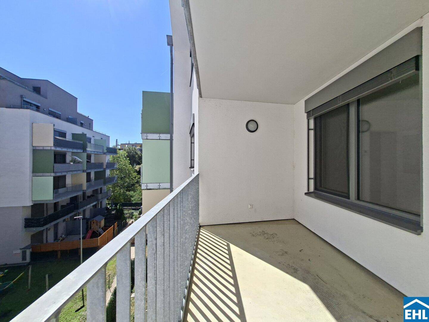 Geräumiger Balkon mit Metallgeländer und Ausblick auf die Wohnanlage und einen Spielplatz.