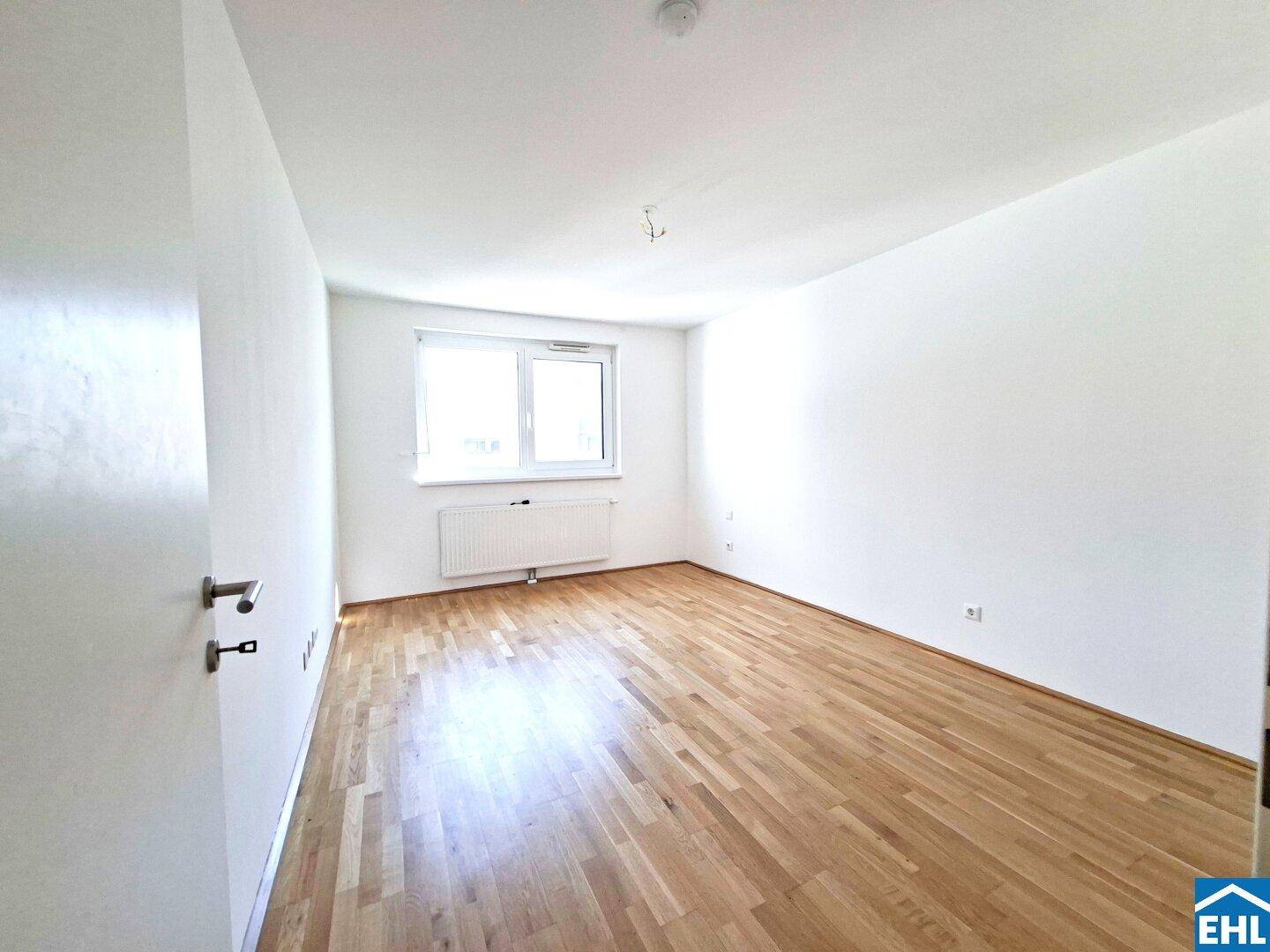 Helles Schlafzimmer mit Parkettboden, weiß gestrichenen Wänden und einem großen Fenster.