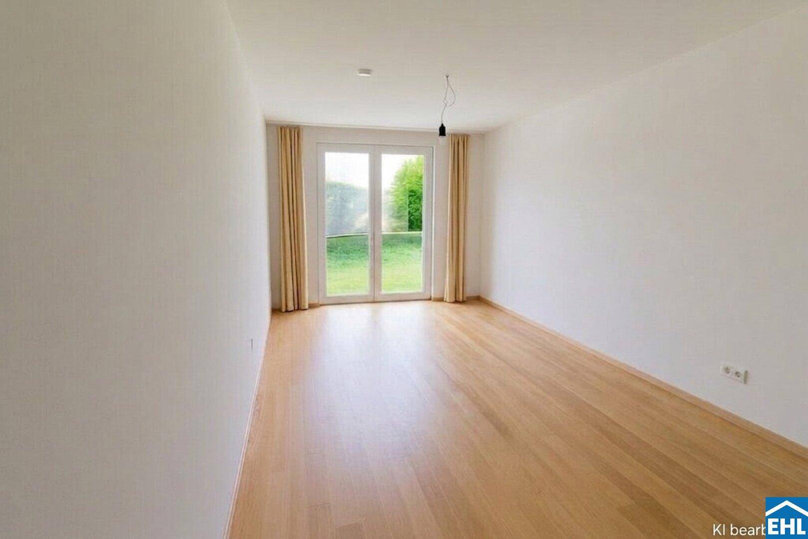 Helles Zimmer mit Holzboden und großen Fenstertüren zum grünen Außenbereich.
