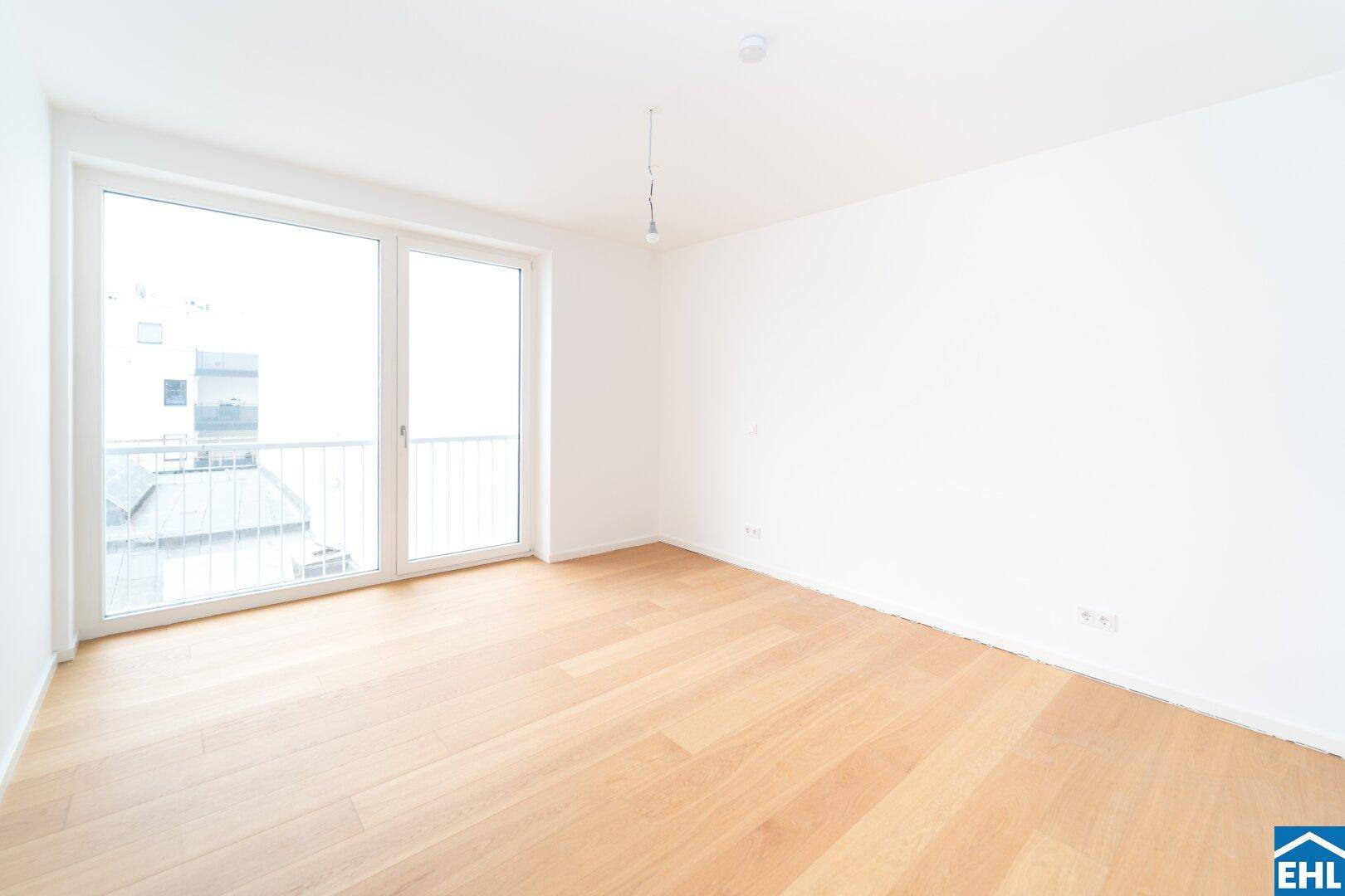 Helles Schlafzimmer mit Holzboden und großem Fenster, das Zugang zu einem Balkon bietet.