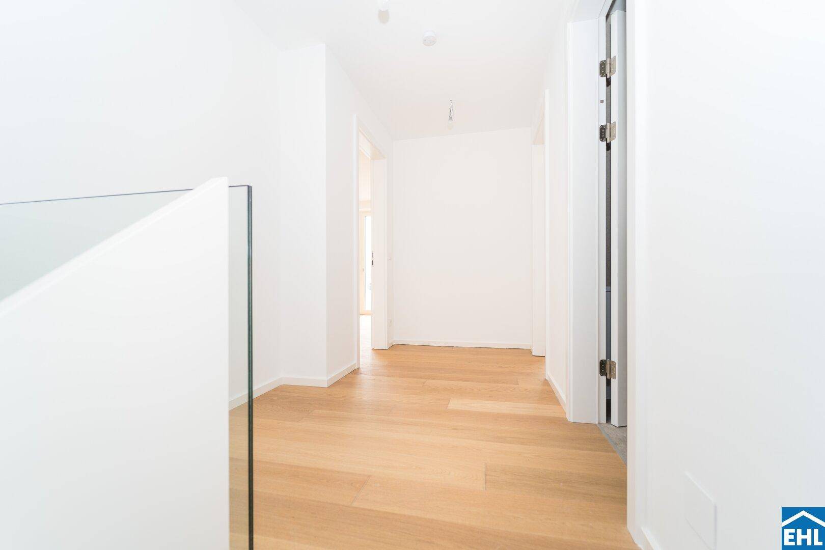 Heller Flur im Obergeschoss mit Holzboden und modernem Glasgeländer, das viel Licht durchlässt.