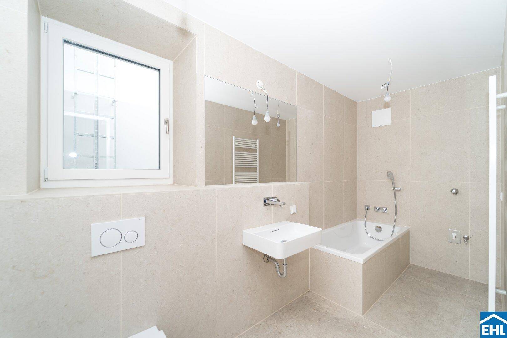 Modernes Badezimmer mit beigefarbenen Fliesen, Badewanne, Waschbecken und Fenster für Tageslicht.