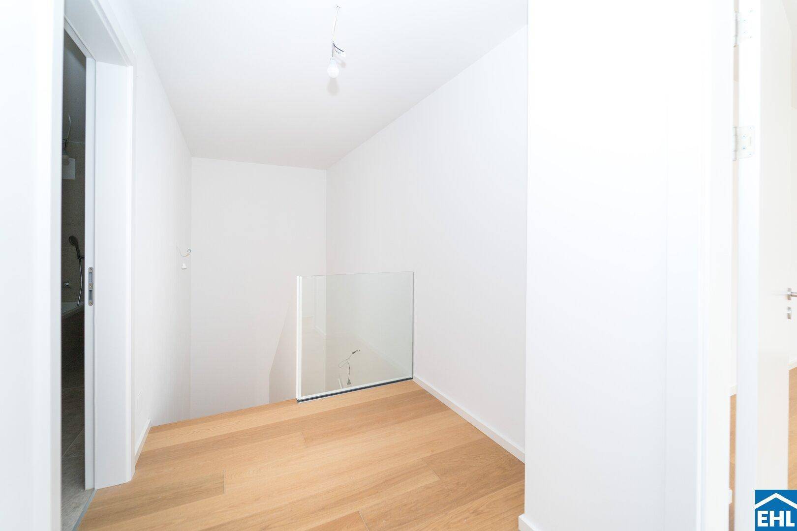 Lichtdurchfluteter Flurbereich mit Holzboden und elegantem Glasgeländer, das den Blick öffnet.