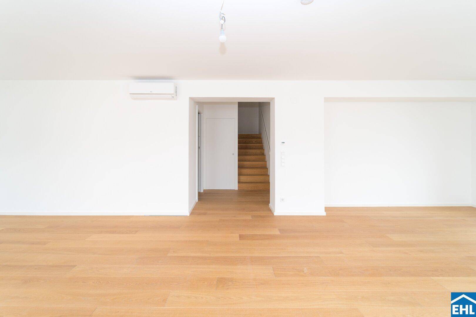 Heller, leerer Raum mit Holzboden und Zugang zu einer Treppe, ideal für ein Wohnzimmer.