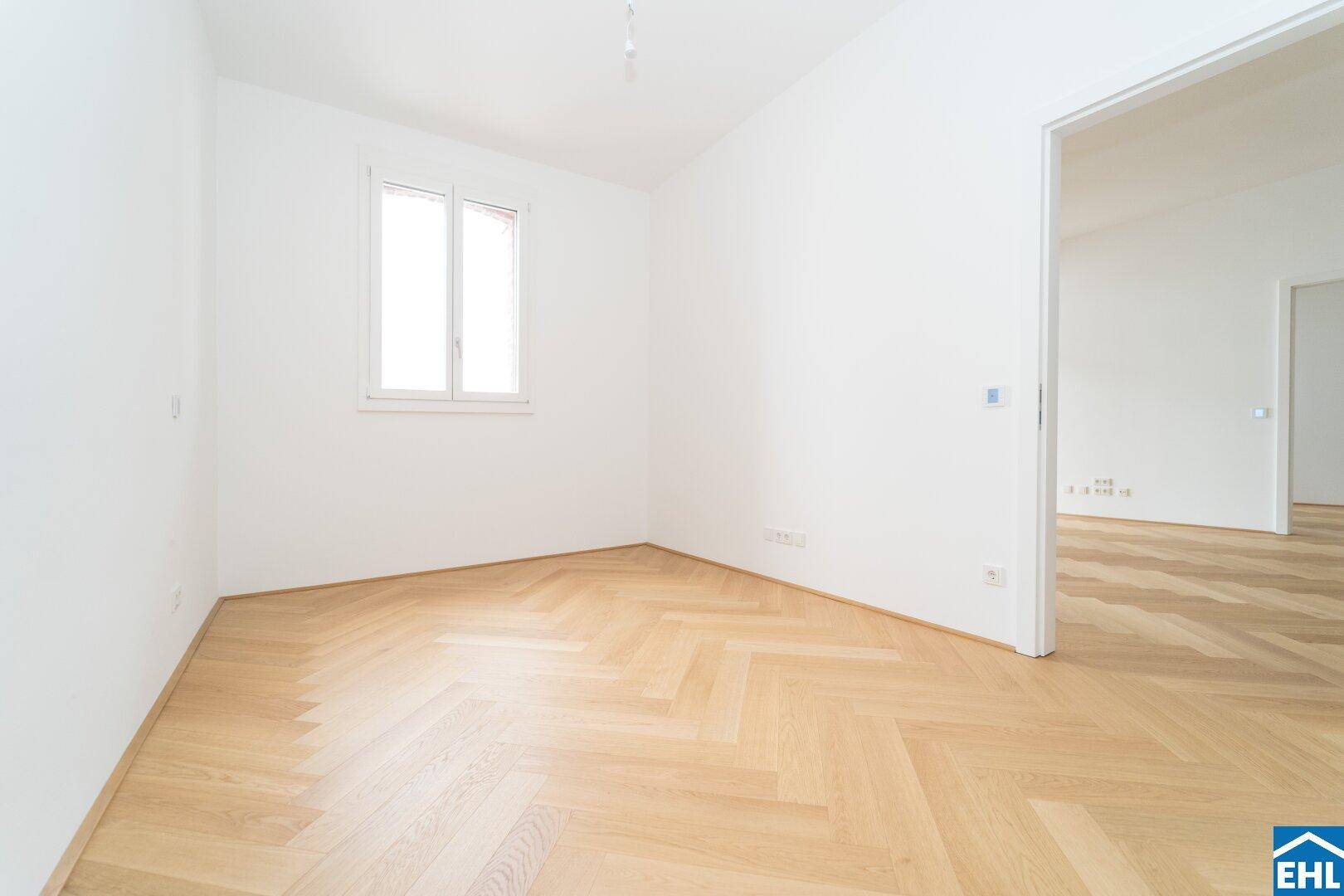Helles Zimmer mit Fischgrätparkett und einem Fenster, ideal als Schlaf- oder Arbeitszimmer.
