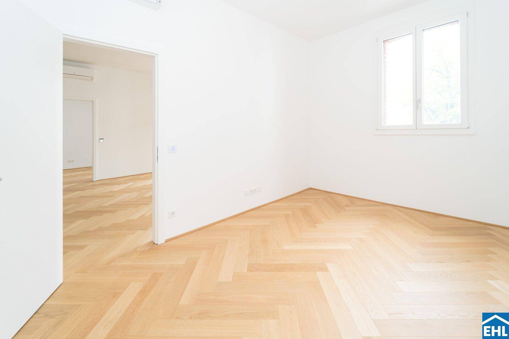 Leeres Zimmer mit Fischgrätparkett und Fenster, bietet vielseitige Nutzungsmöglichkeiten.