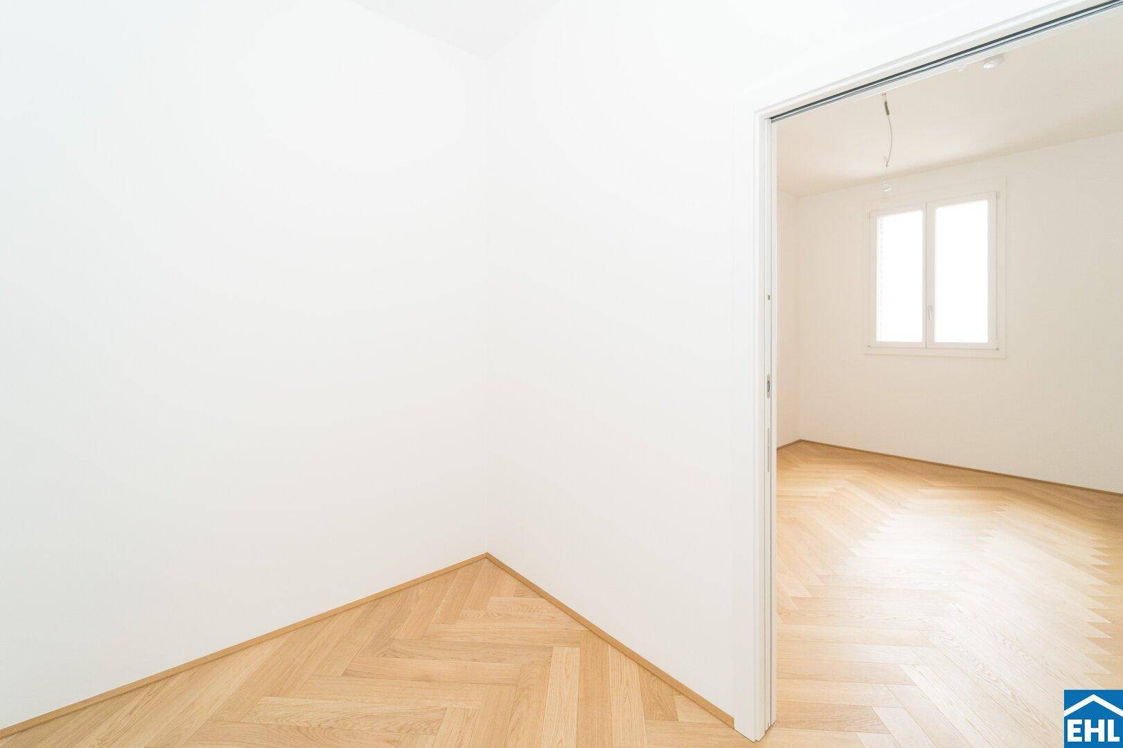 Heller Durchgangsbereich mit Fischgrätparkett, der zu einem weiteren Zimmer führt.