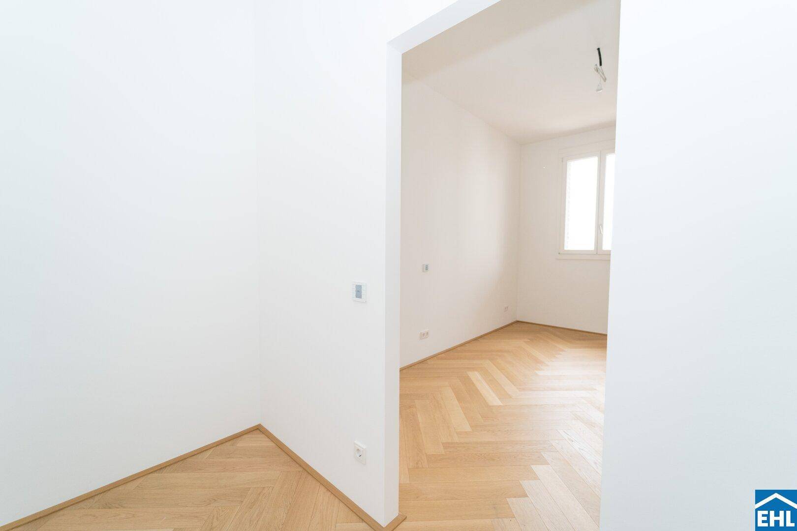 Eingangsbereich oder Flur mit Fischgrätparkett, der den Blick in ein helles Zimmer freigibt.