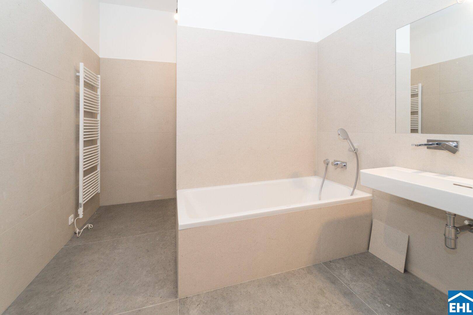 Modernes Badezimmer mit beigefarbenen Fliesen, Badewanne und beheiztem Handtuchhalter.