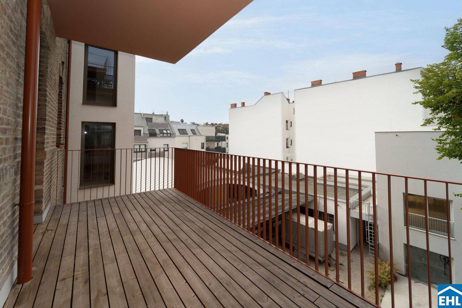 Langer Balkon mit Holzdielen und Blick auf die umliegenden Wohngebäude.