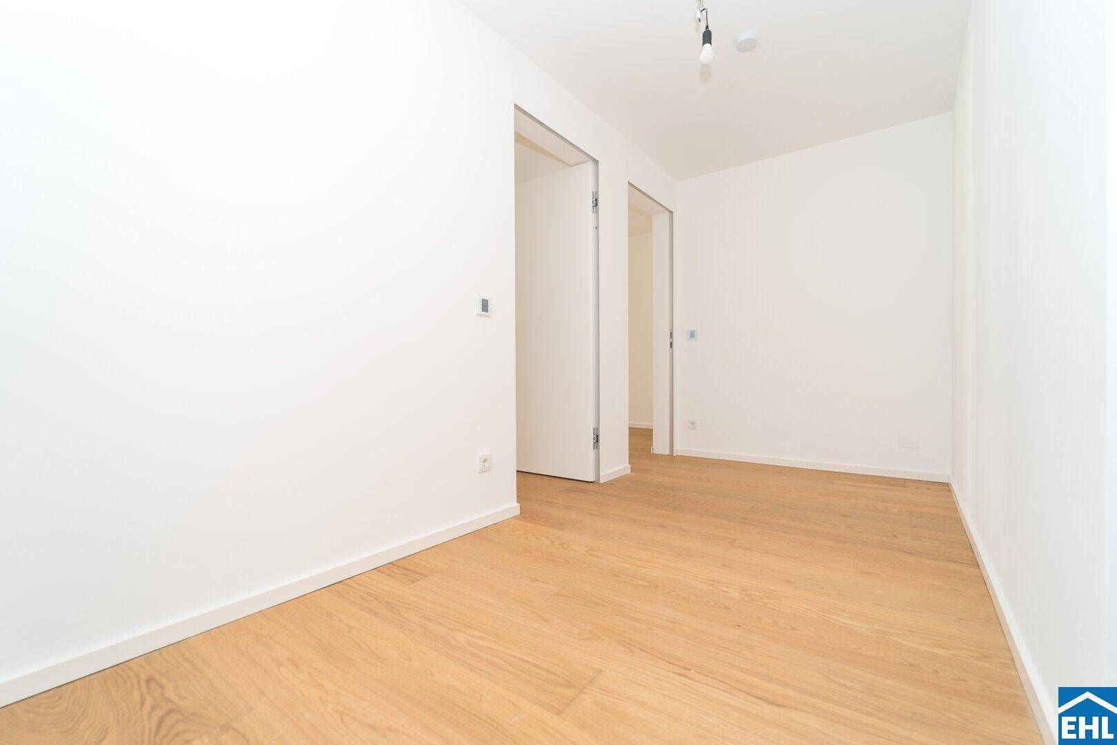 Leeres Zimmer mit hellem Holzboden und zwei offenen Türen, bereit zur individuellen Gestaltung.