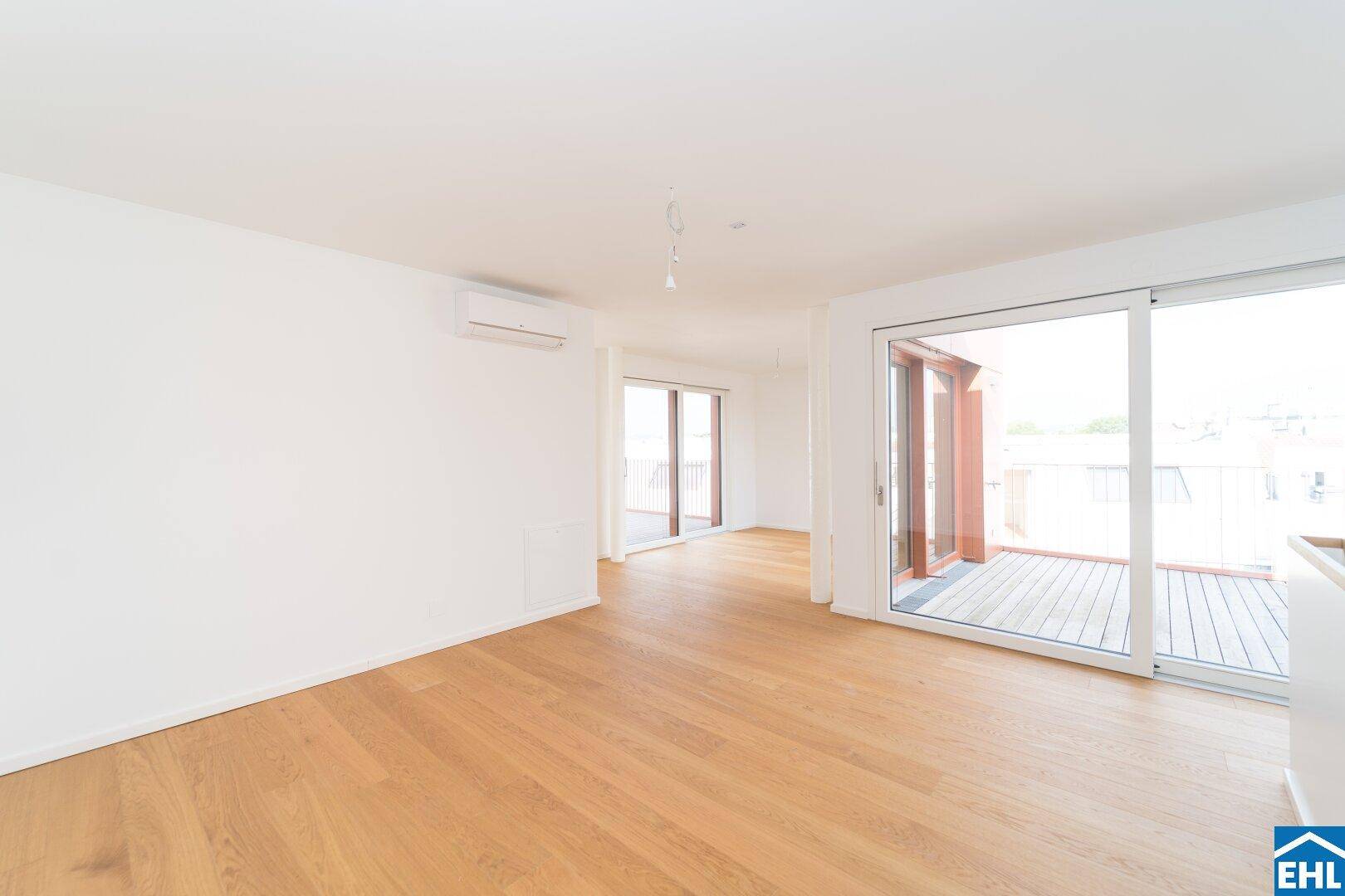 Helles, leeres Zimmer mit Holzboden und Zugang zu einem Balkon, ausgestattet mit Klimaanlage.