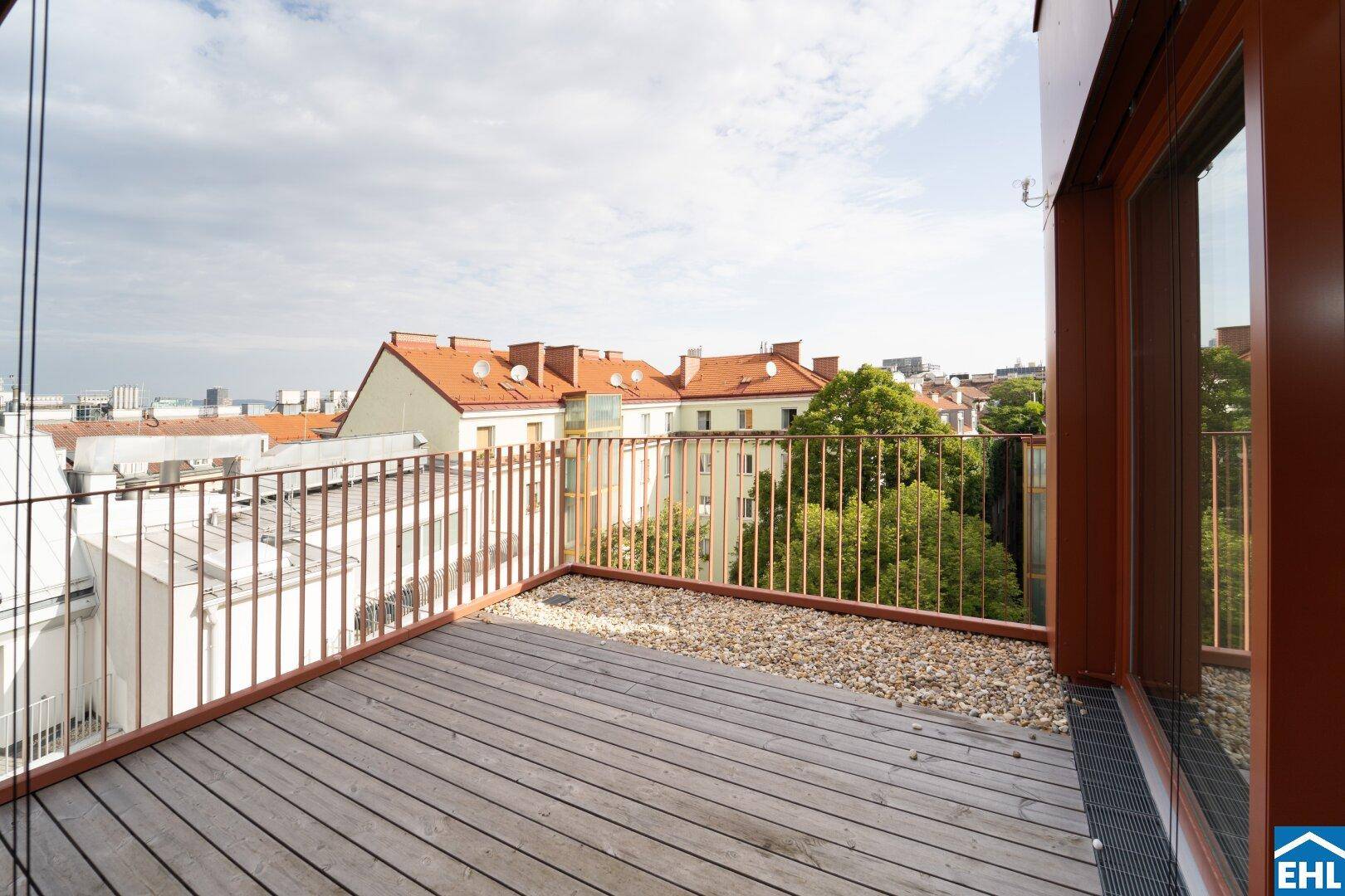 Geräumiger Balkon mit Holzboden und Metallgeländer, bietet einen Blick über die Dächer der Stadt.