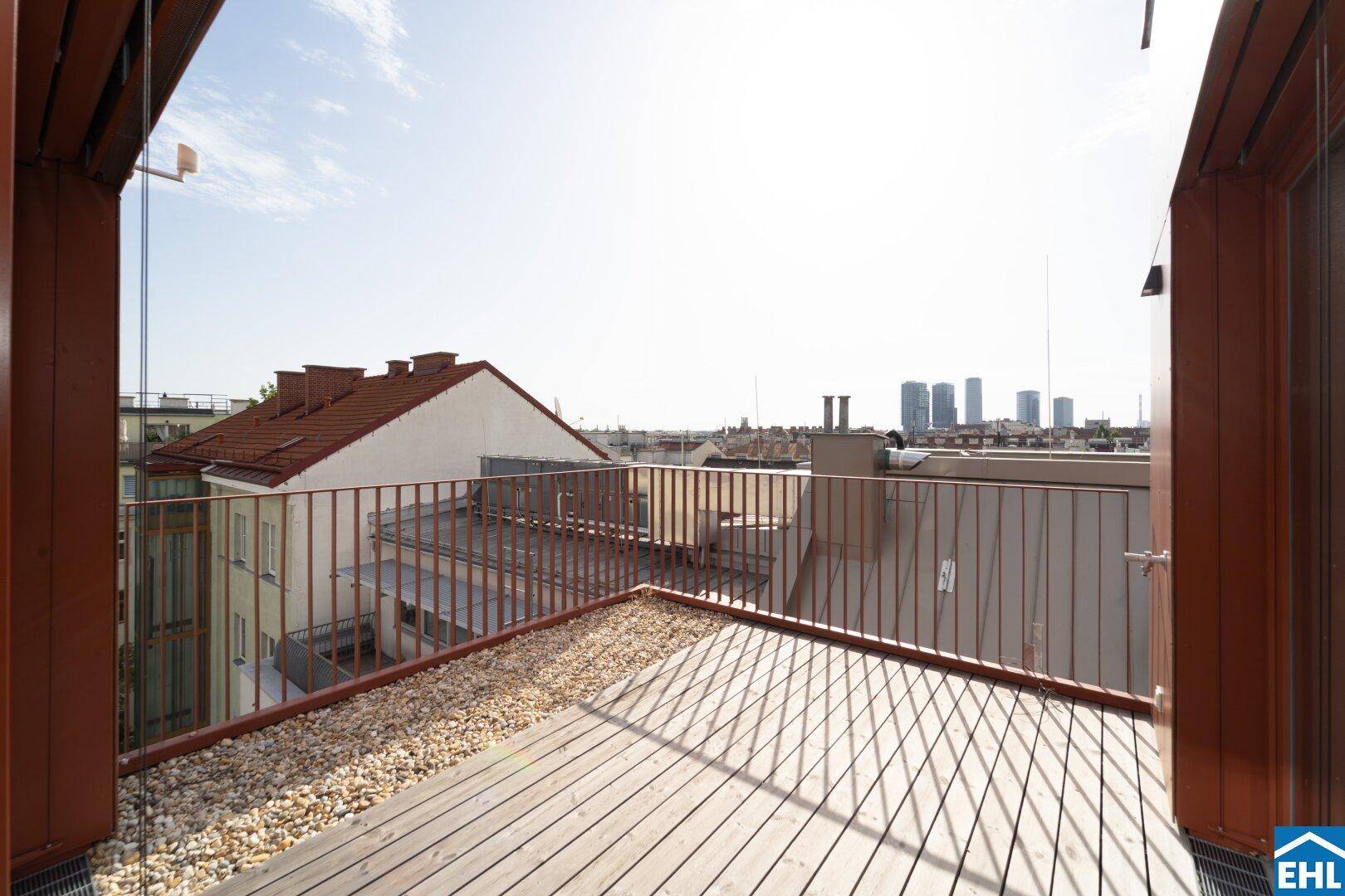 Dachterrasse mit Holzboden, Kiesbereich und Blick auf die Stadtkulisse.