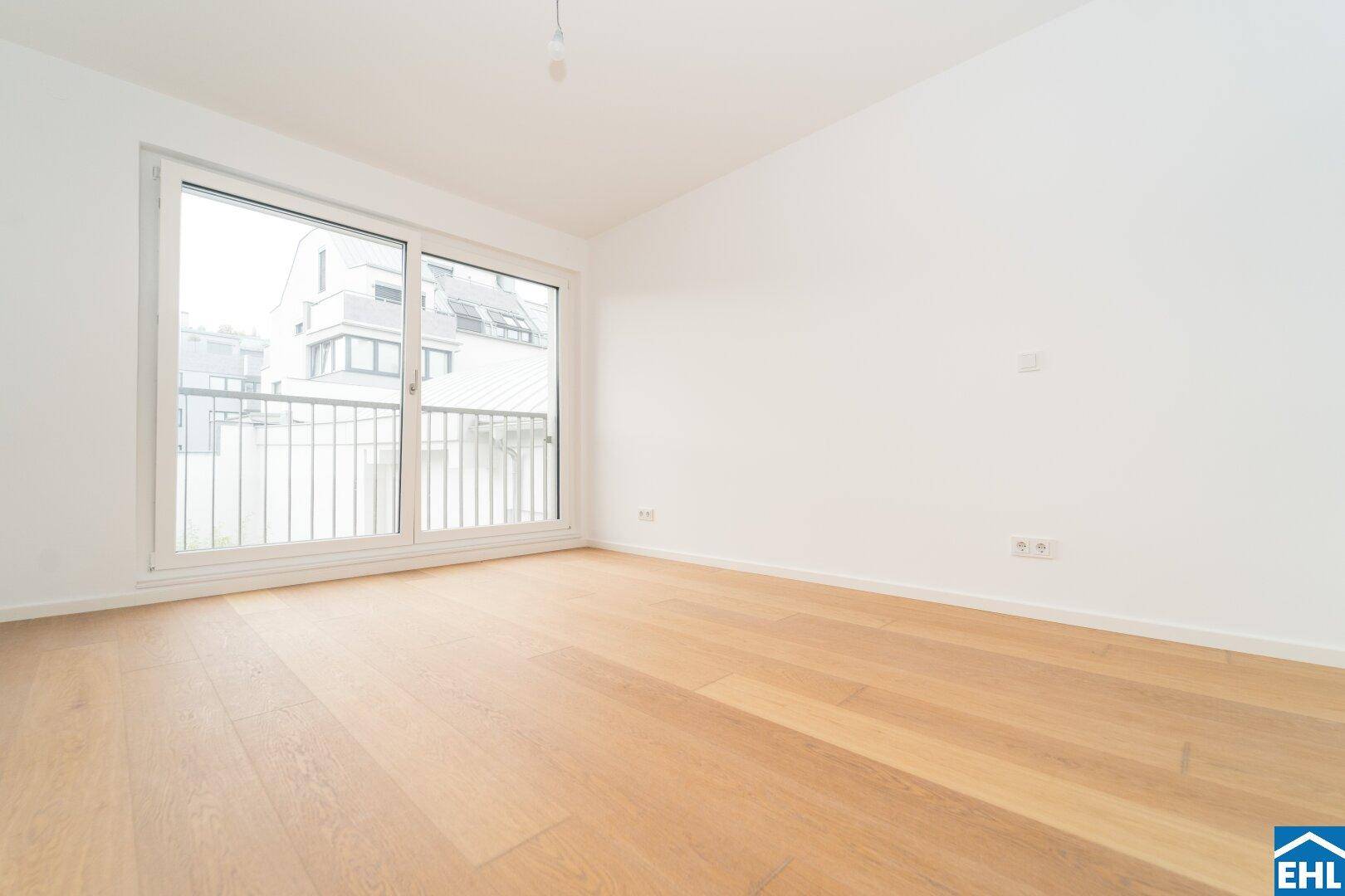 Helles Zimmer mit Holzboden und Blick auf die umliegenden Gebäude durch große Fenster.